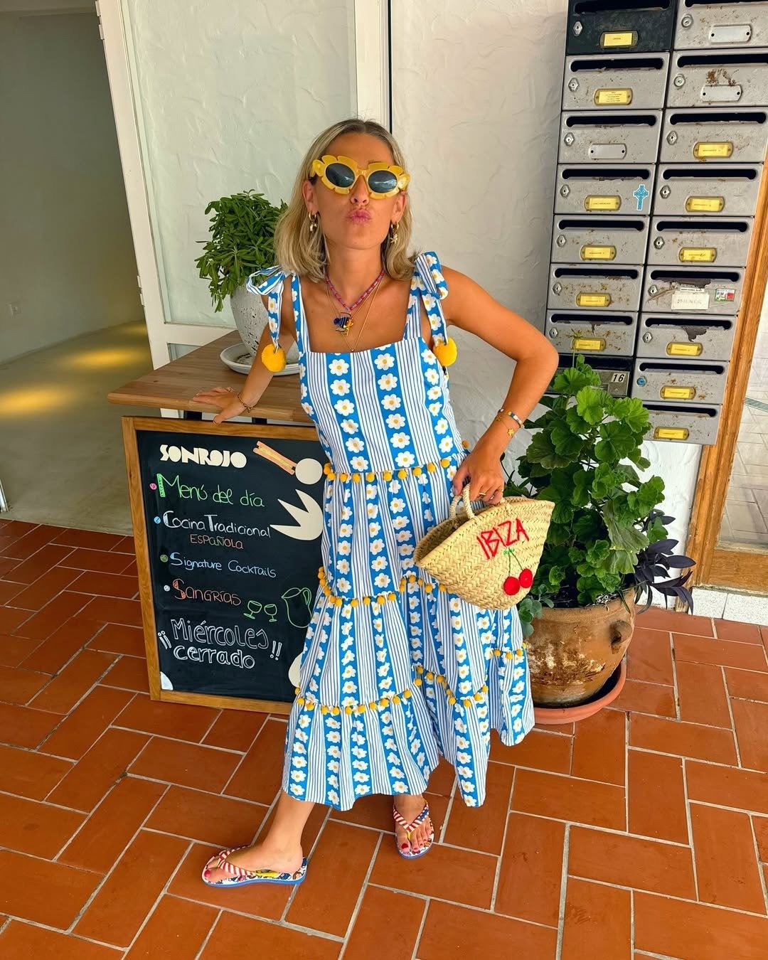 A imagem apresenta uma mulher usando um vestido longo azul com estampas florais e listras, ideal para dias quentes. Ela combina o look com um chinelo azul, que traz conforto e estilo.