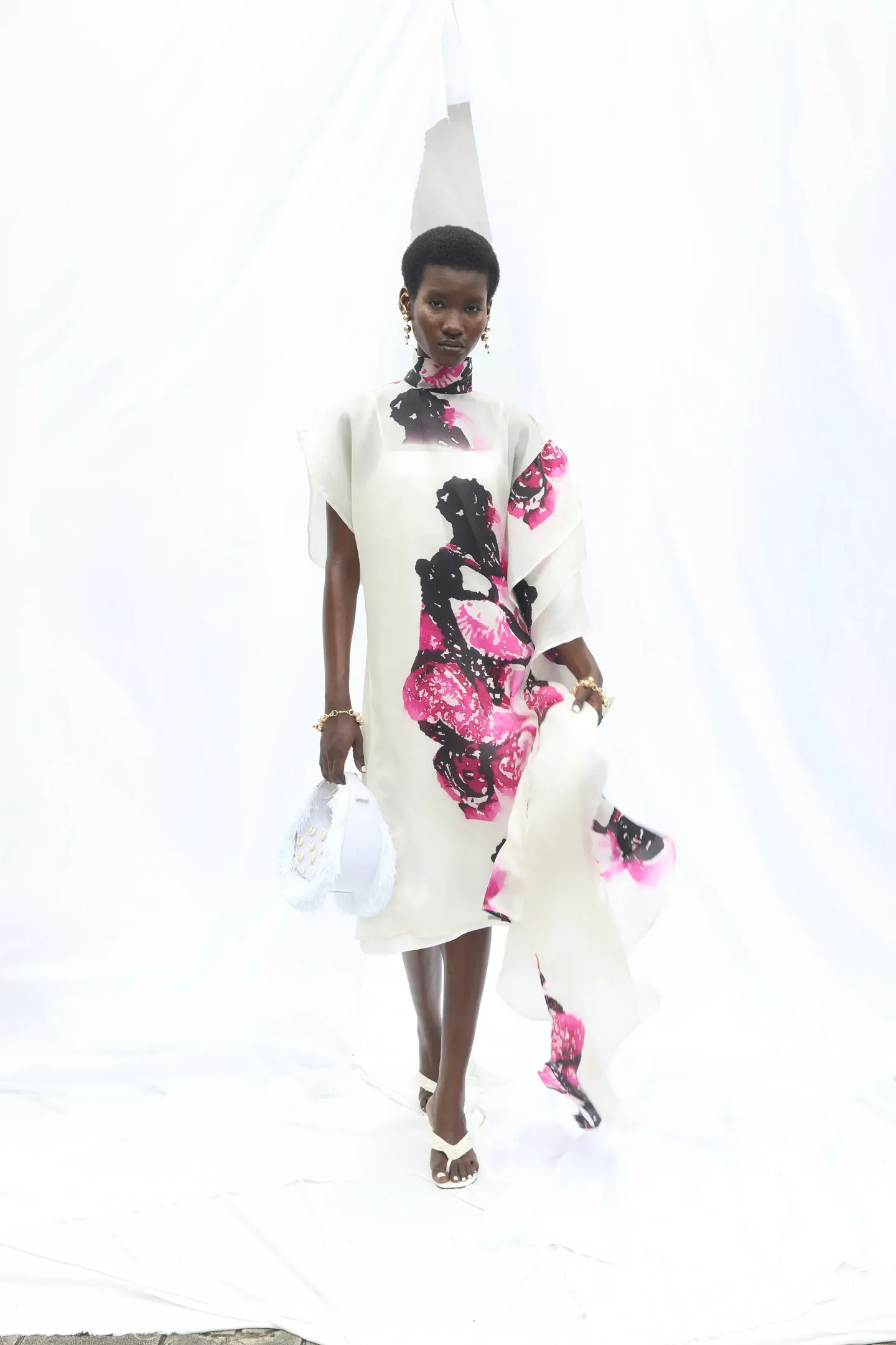 Durante a Lagos Fashion Week, uma modelo exibe um vestido elegante em tons de branco, negro e rosa. O design conta com estampas artísticas e fluídas, destacando a leveza da peça.