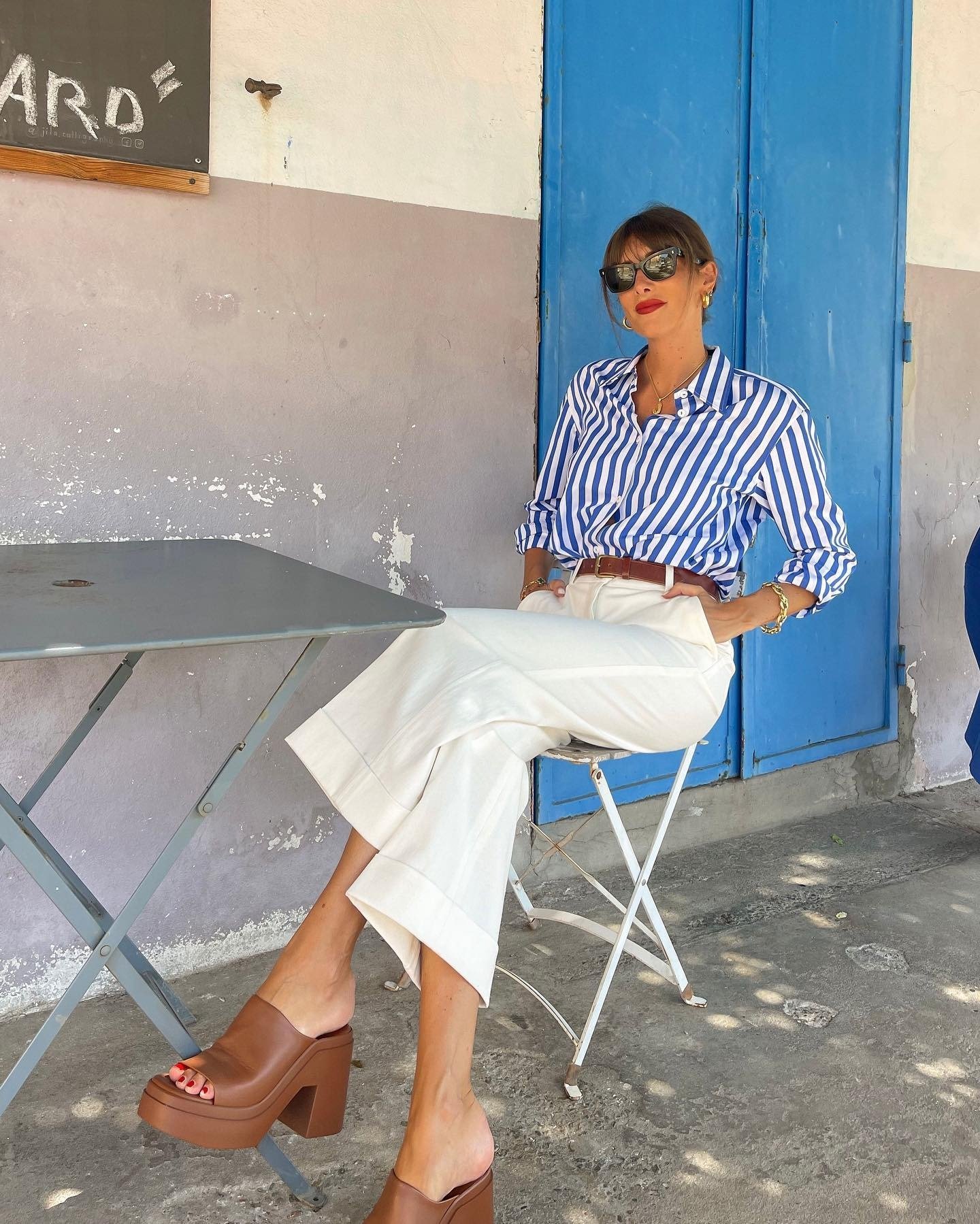 Look com pantacourt branca de tecido estruturado combinada a camisa listrada azul e branca, salto marrom e acessórios