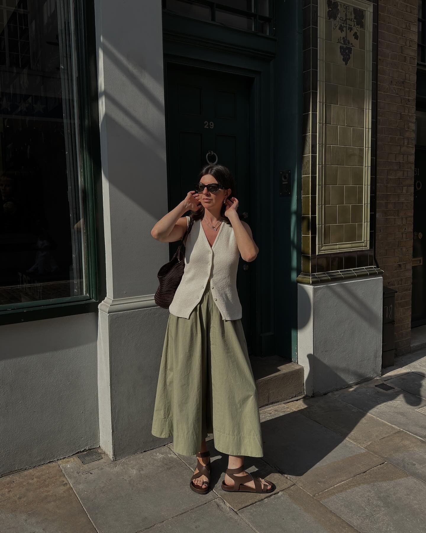 Look com pantacourt verde claro em tecido leve, combinado com colete off-white de tricô e sandálias marrons, modelo ajusta o