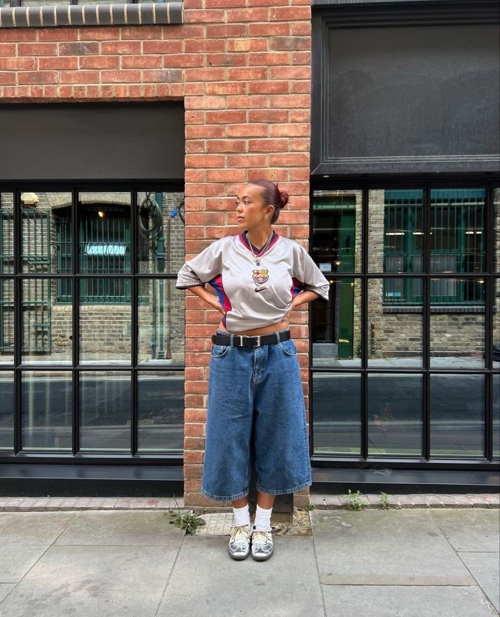 Look com pantacourt jeans de modelagem ampla combinado a camiseta esportiva cinza com detalhes em vermelho, postura