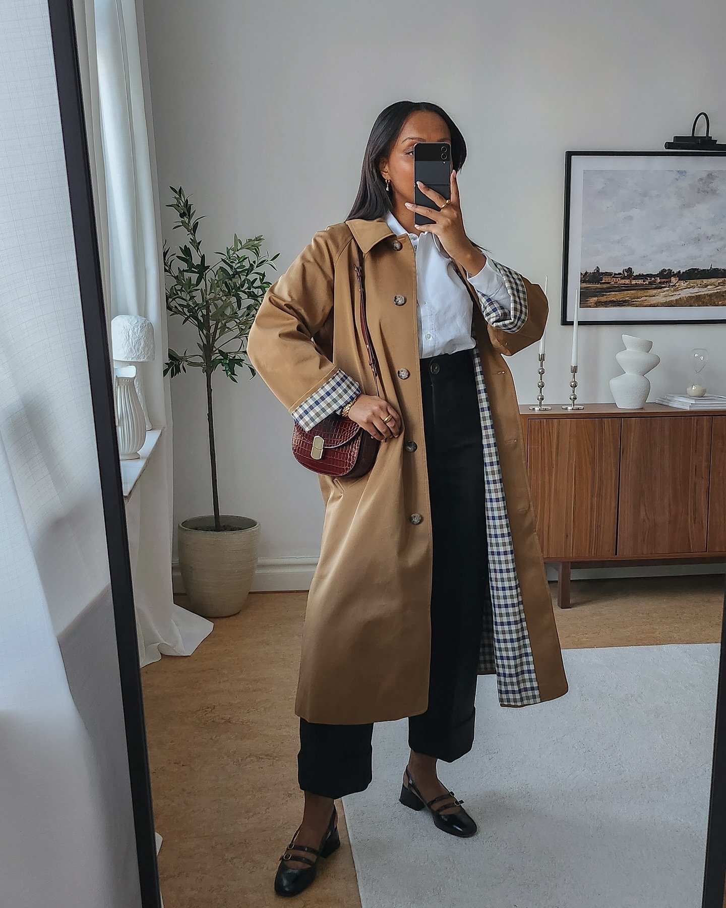 Modelo posa com look com pantacourt preta de tecido estruturado, camisa branca e sobretudo camel com forro xadrez, em