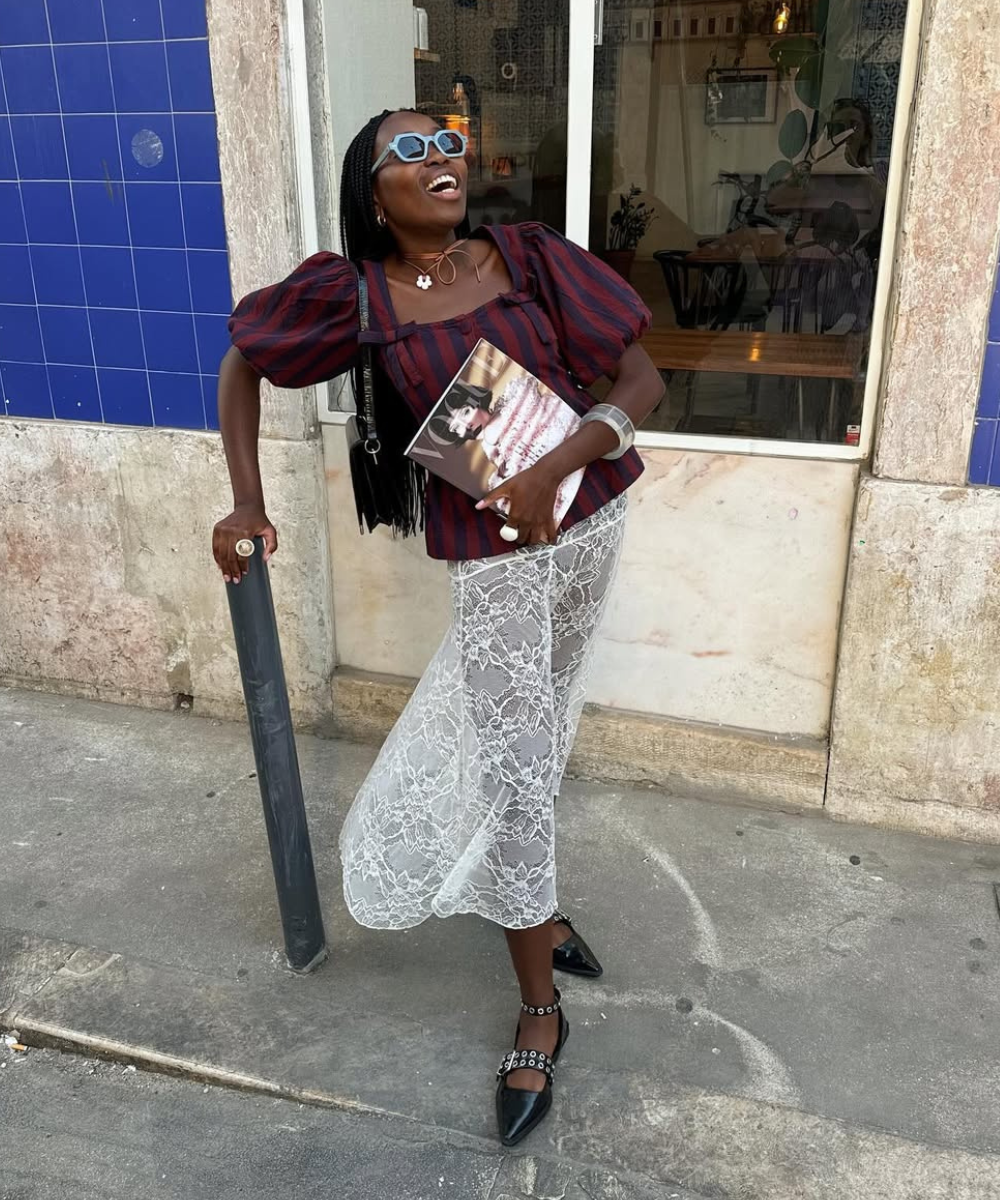 Modelo sorri e posa com saia rendada branca transparente, blusa listrada vinho e preta de mangas bufantes, acessórios