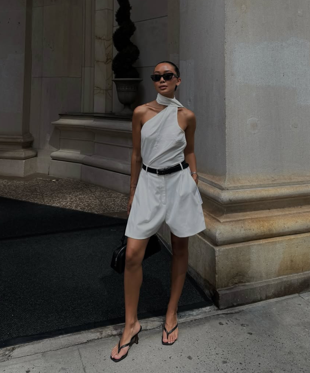 Look esporte fino com macaquinho branco de tecido fluido, modelagem ampla, cinto preto, sandálias de tiras finas e óculos