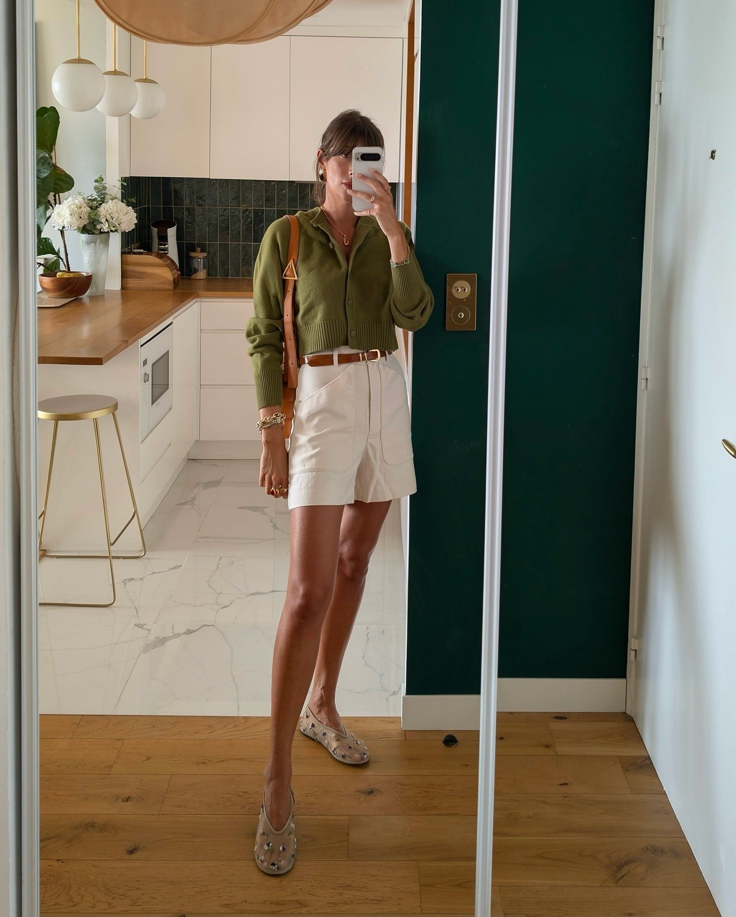 Modelo posa em look natal verde com cardigan cropped de tricô, shorts off-white e acessórios em tons terrosos, transmitindo