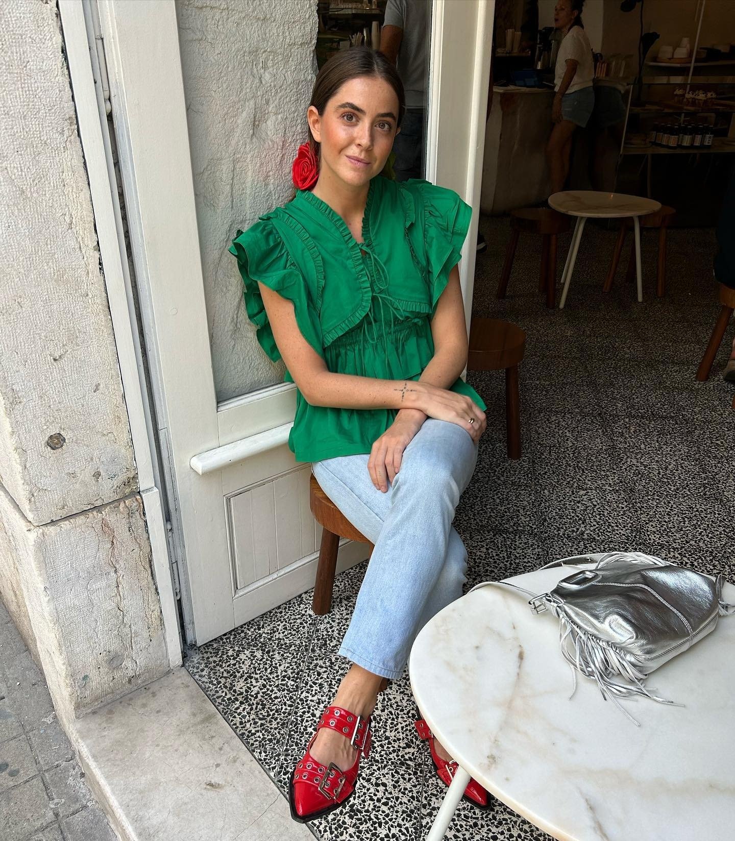 Look natal verde com blusa de algodão com babados, jeans claro, sapatos vermelhos e acessório floral, transmitindo charme e