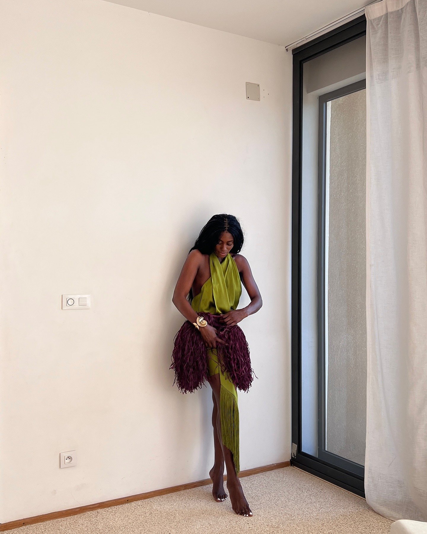 Look natal verde com vestido de cetim drapeado e saia de franjas vinho, modelo ajusta a peça em pose delicada e elegante.