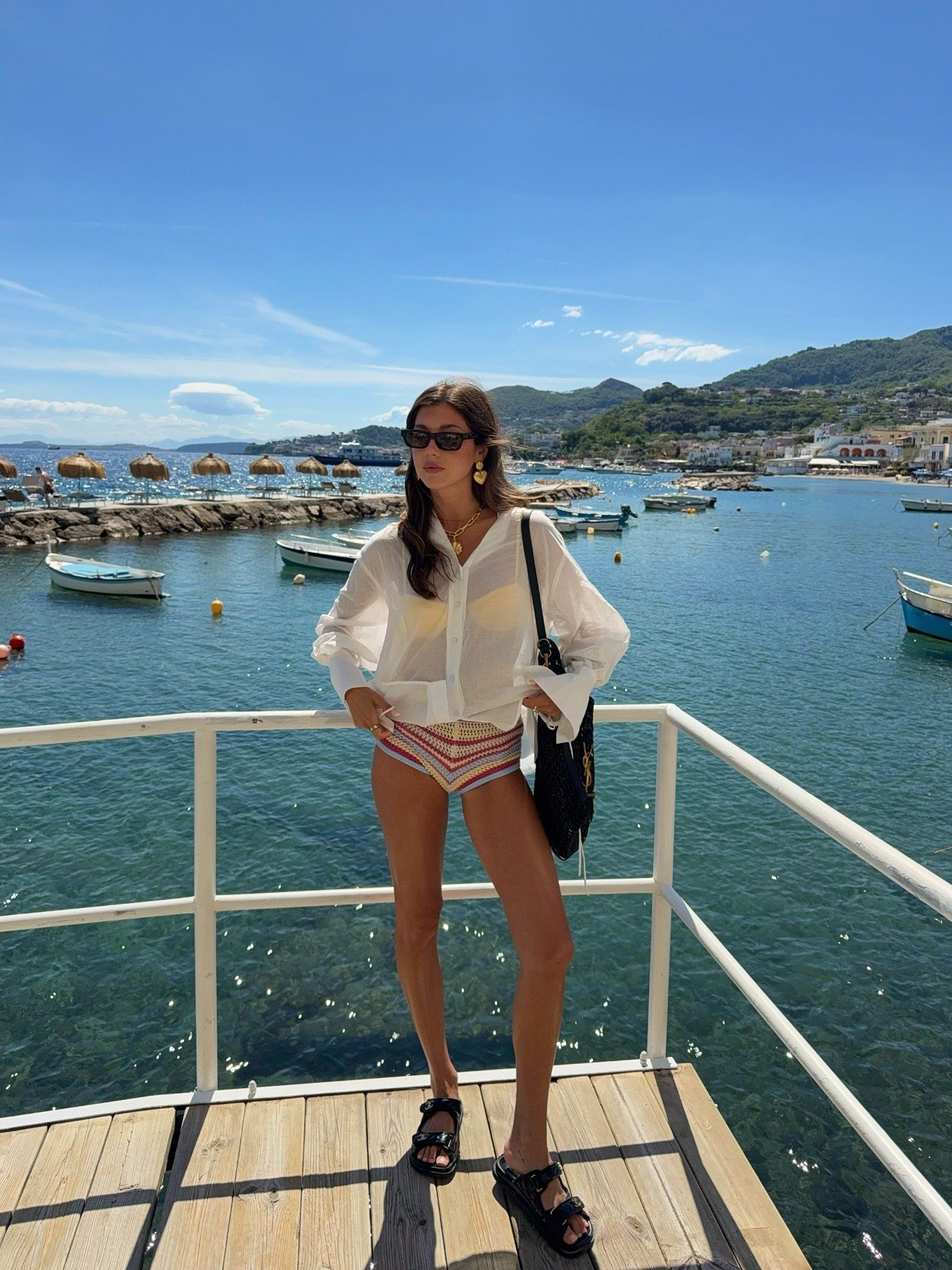 O look praia para o verão 2026 combina elegância e praticidade. A modelo exibe uma camisa branca leve, ideal para dias quentes, sobre um biquíni de crochê colorido, que traz um toque vibrante.