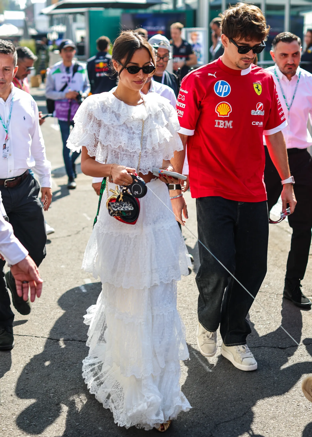 Alexandra Saint Mleux exibe um look sofisticado e romântico com um vestido branco de camadas, adornado com detalhes de renda. Ela complementa a produção com óculos escuros elegantes e uma bolsa charmosa.