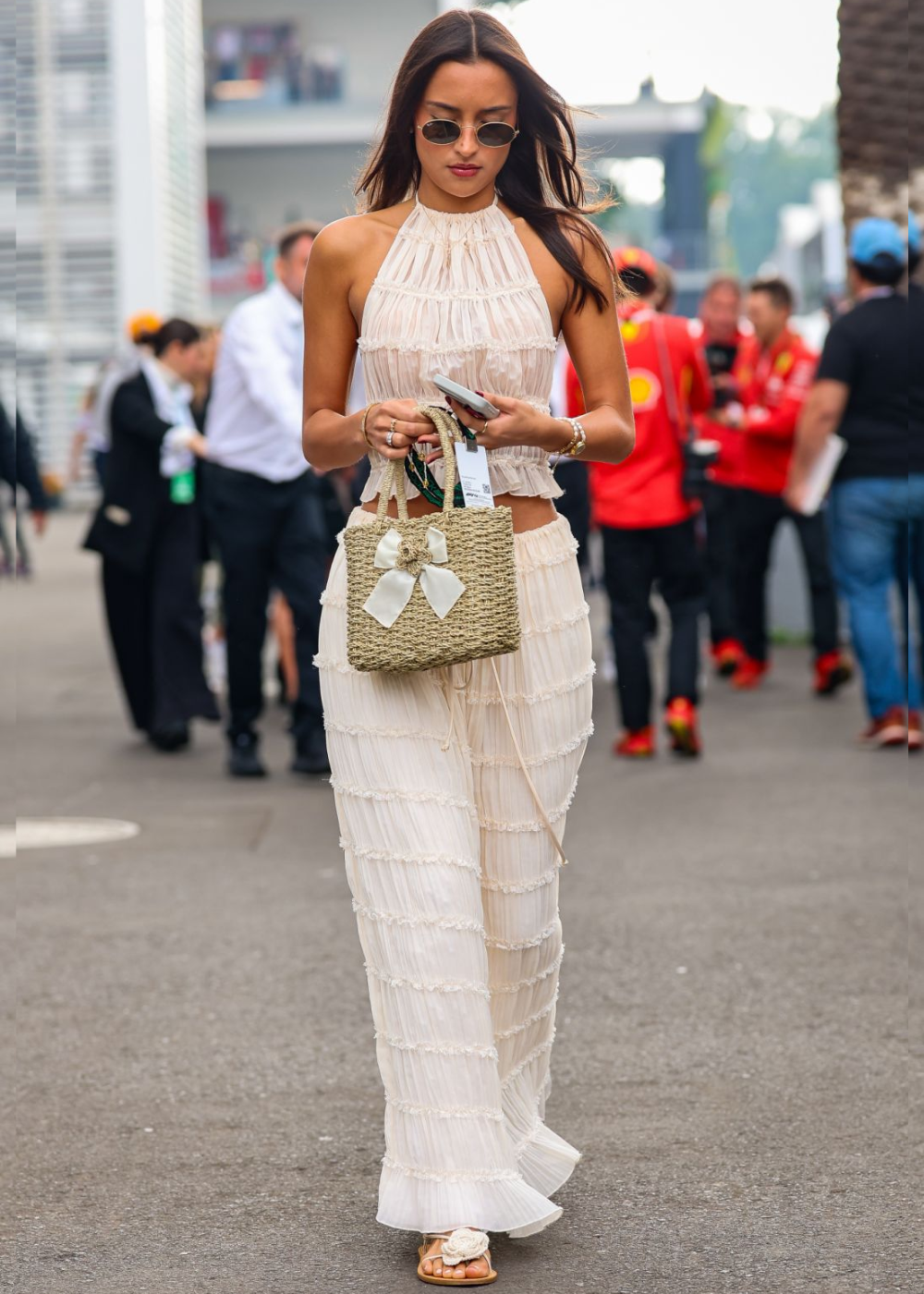 Alexandra Saint Mleux exibe um look sofisticado e leve, composto por um conjunto de top e calça de tecido plissado em tom claro. O top, com decote halter, destaca os ombros e combina com a calça fluida, que apresenta detalhes de babados.