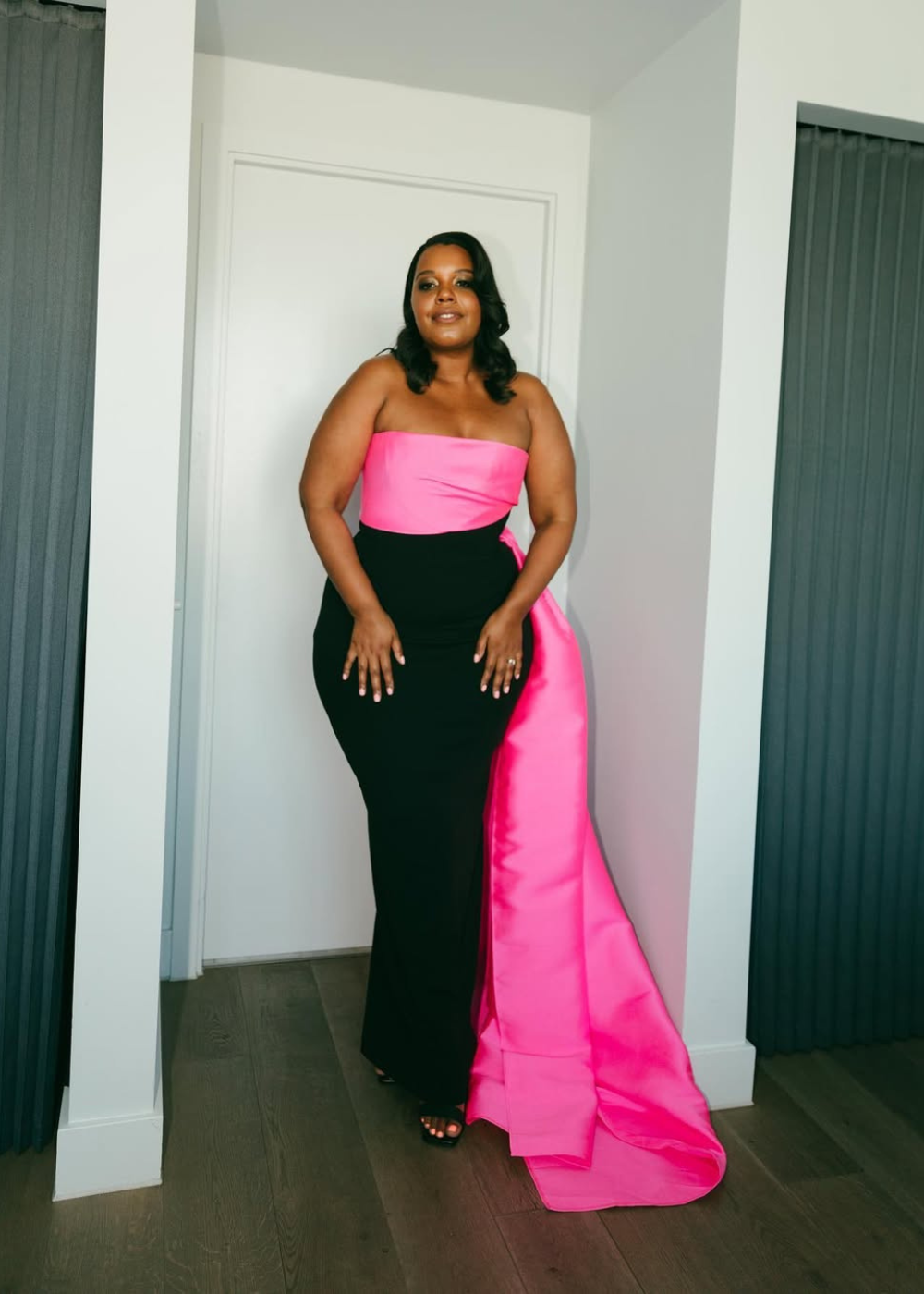 Modelo posa com look black tie em vestido longo tomara que caia com corpo preto justo e detalhe em tecido rosa vibrante que