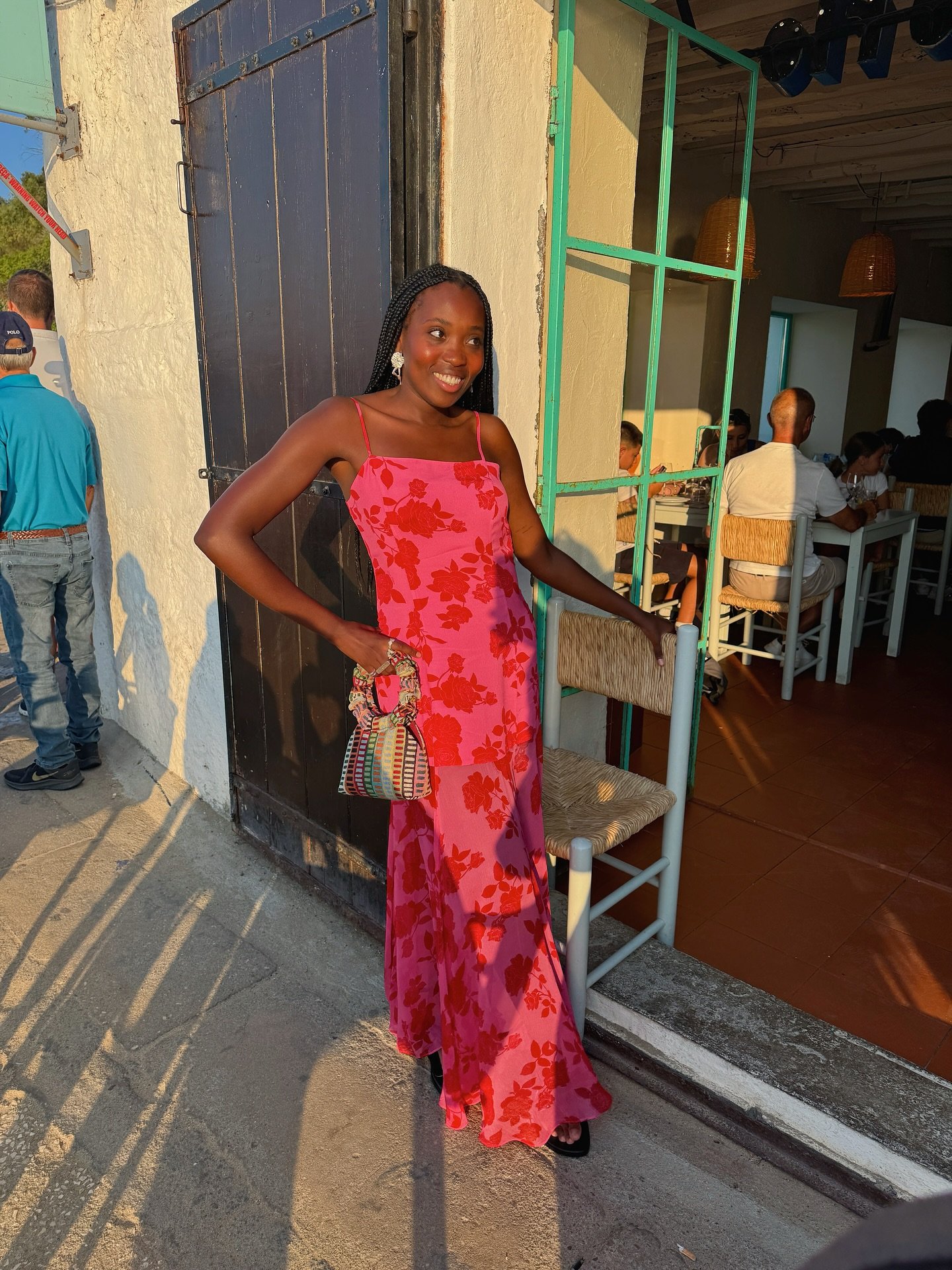 Vestido tendência longo rosa com estampa floral vermelha, modelagem fluida e alças finas, modelo posa sorrindo em luz