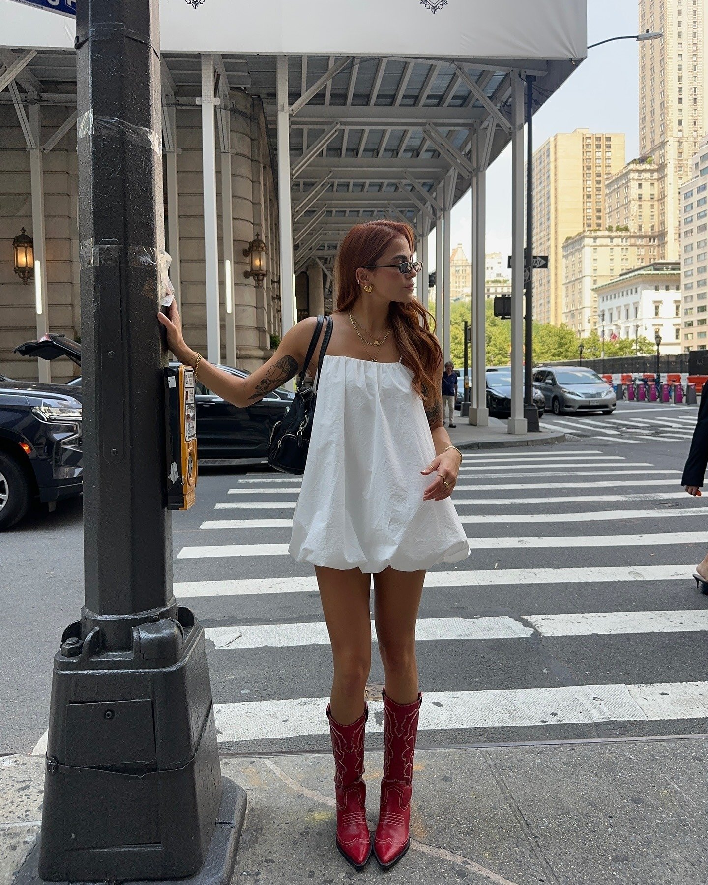 Modelo posa com vestido branco curto de tecido leve e bota cano alto vermelha em estilo western, criando look urbano e