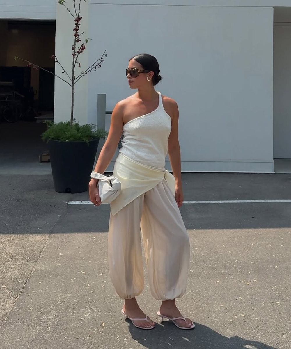Looks com calça balonê bege em tecido fluido, regata assimétrica branca e sandália delicada, transmitindo leveza e