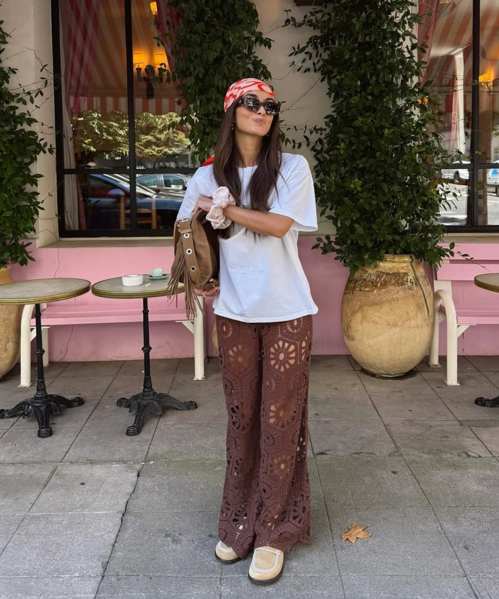 Modelo posa com look com crochê em calça marrom de trama aberta, camiseta branca oversized e lenço vermelho na cabeça,