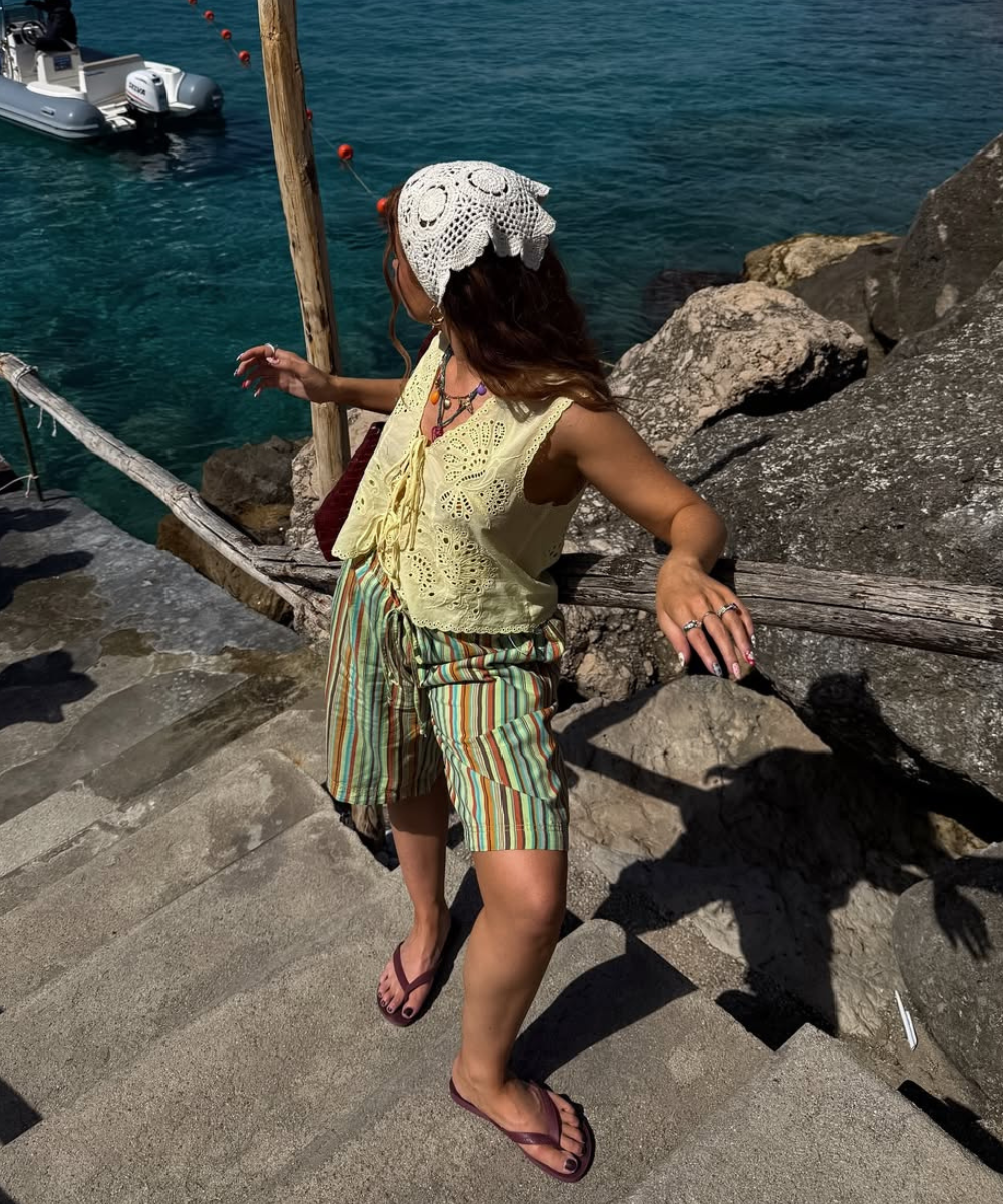 Look com crochê em colete amarelo claro de textura delicada, short listrado e bandana branca, clima leve e praiano.