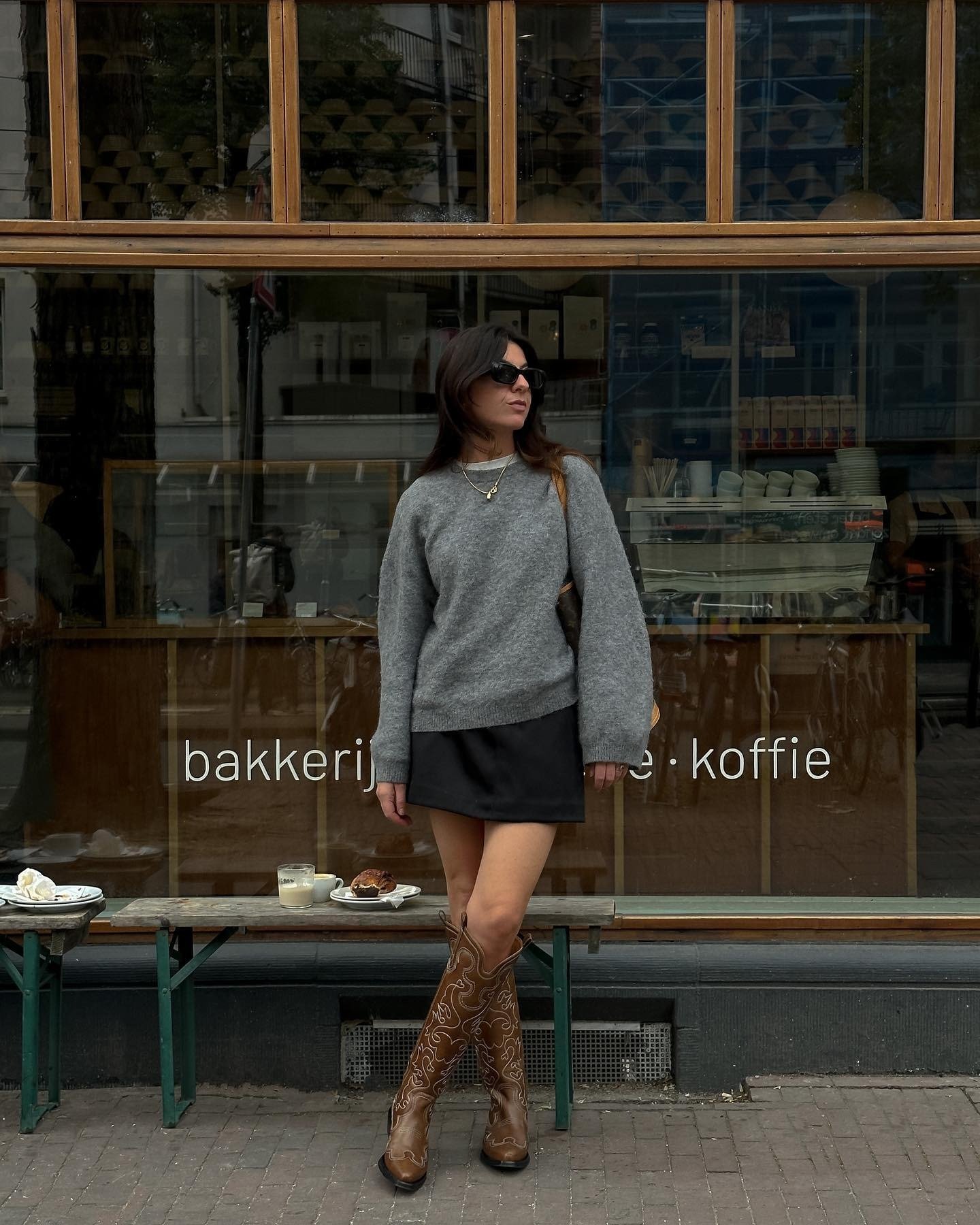 O look com saia preta curta destaca-se pela combinação de estilo e conforto. A peça, que possui um corte moderno, é complementada por um suéter cinza oversized, perfeito para dias mais frescos.