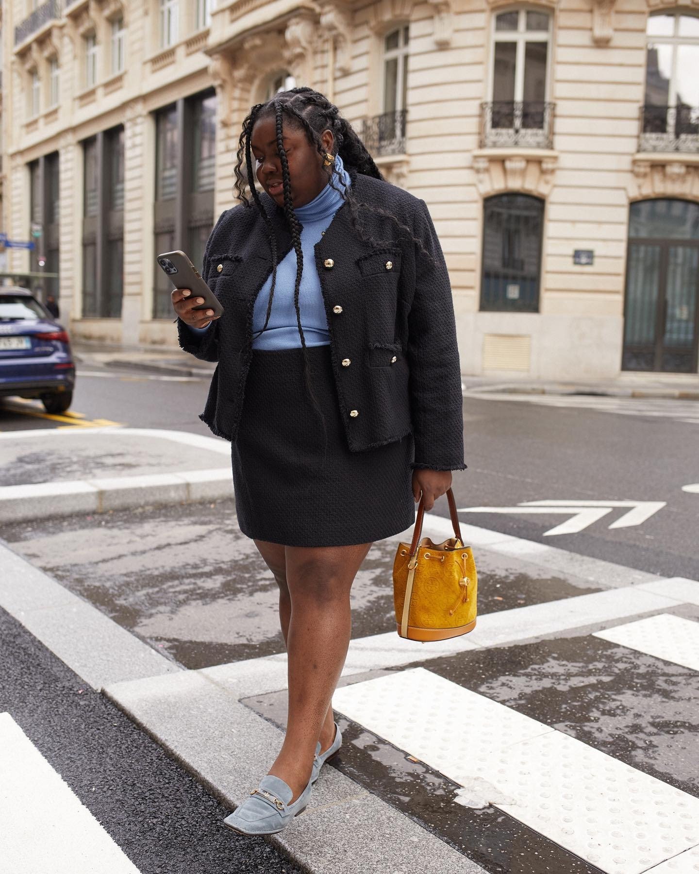 O look com saia preta curta destaca-se pela combinação elegante e moderna. A saia é acompanhada por um blazer preto texturizado, que adiciona sofisticação. A blusa azul clara traz um toque de cor, equilibrando o visual.