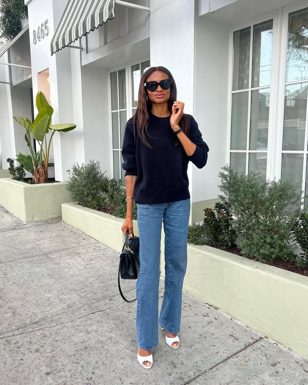O sapato peep-toe branco destaca-se na composição do look, trazendo um toque de elegância. A modelo usa uma blusa preta e calça jeans flare, criando um contraste sofisticado.