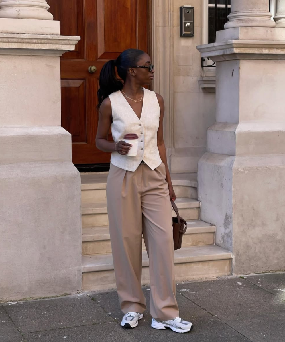 O look apresenta uma combinação elegante de peças que trazem conforto e estilo. A modelo usa um colete claro sobre uma blusa simples, combinado com calças largas em tom bege.