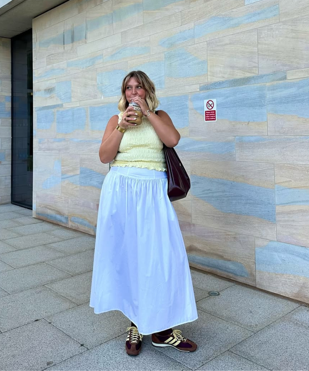 A imagem apresenta um look estiloso que combina conforto e elegância. A mulher usa um top amarelo claro com detalhes franzidos e uma saia longa branca, criando um contraste fresco e leve.