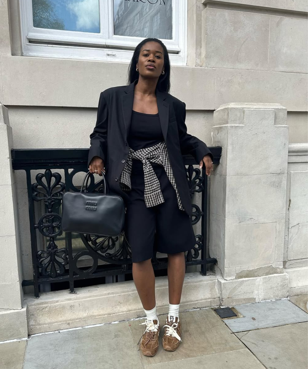 Look moderno e descomplicado com tênis, combinando um blazer oversized preto e uma blusa preta básica. O toque de estilo vem do short preto e da camisa xadrez amarrada na cintura.