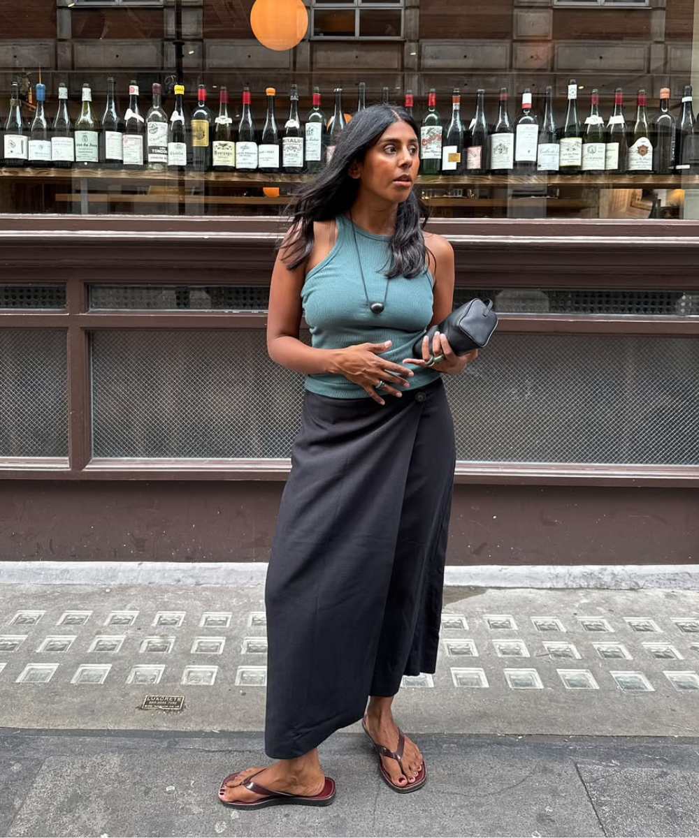 Modelo posa com regata verde musgo de malha canelada e saia envelope preta em tecido leve, completando look fácil de calor