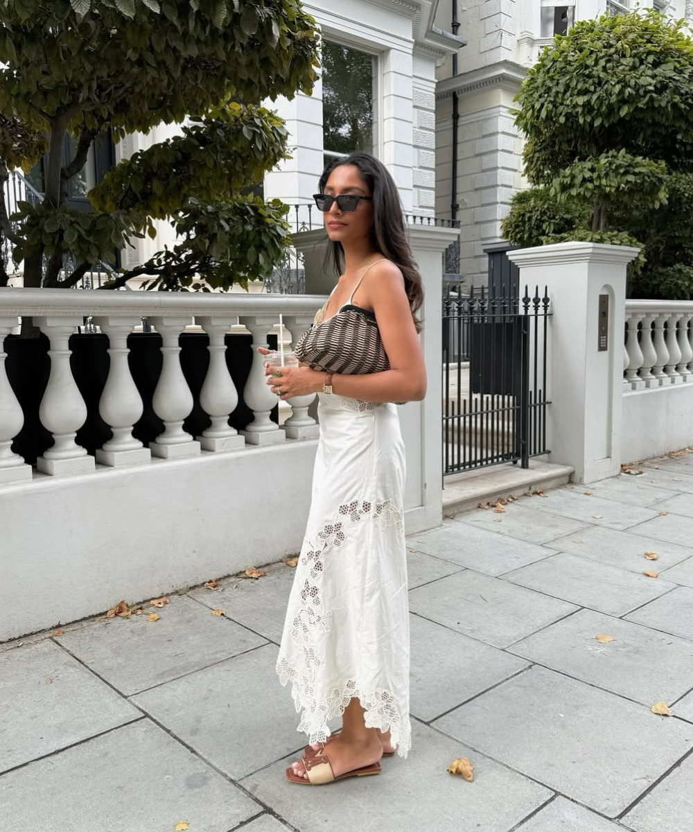 Modelo posa ao ar livre com top de alças finas em tricô marrom e bege, saia branca longa com bordados vazados e sandálias