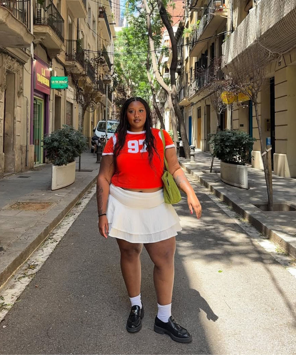 Modelo posa na rua com looks fáceis de calor usando camiseta cropped vermelha, saia branca de tecido leve e sapatos pretos