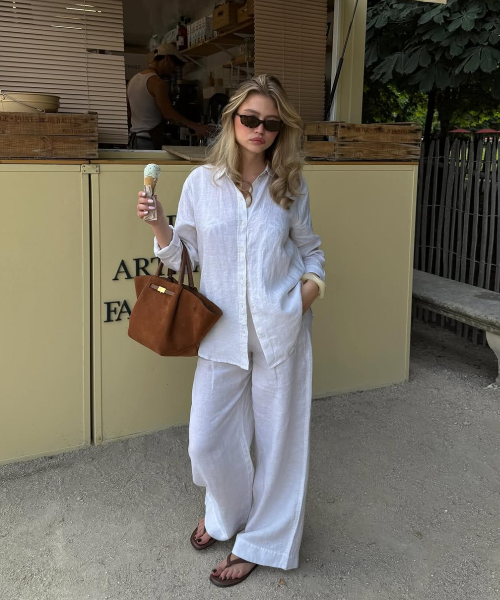 Modelo posa com looks fáceis de calor em conjunto branco de linho fluido, sandálias rasteiras e bolsa marrom de couro,