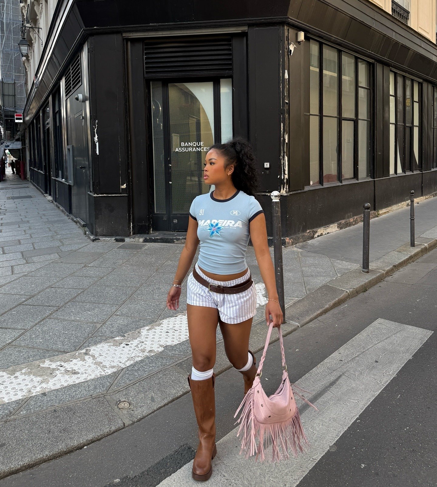 Ideias de looks femininos que combina camiseta azul clara justa, shorts listrados, botas marrons.