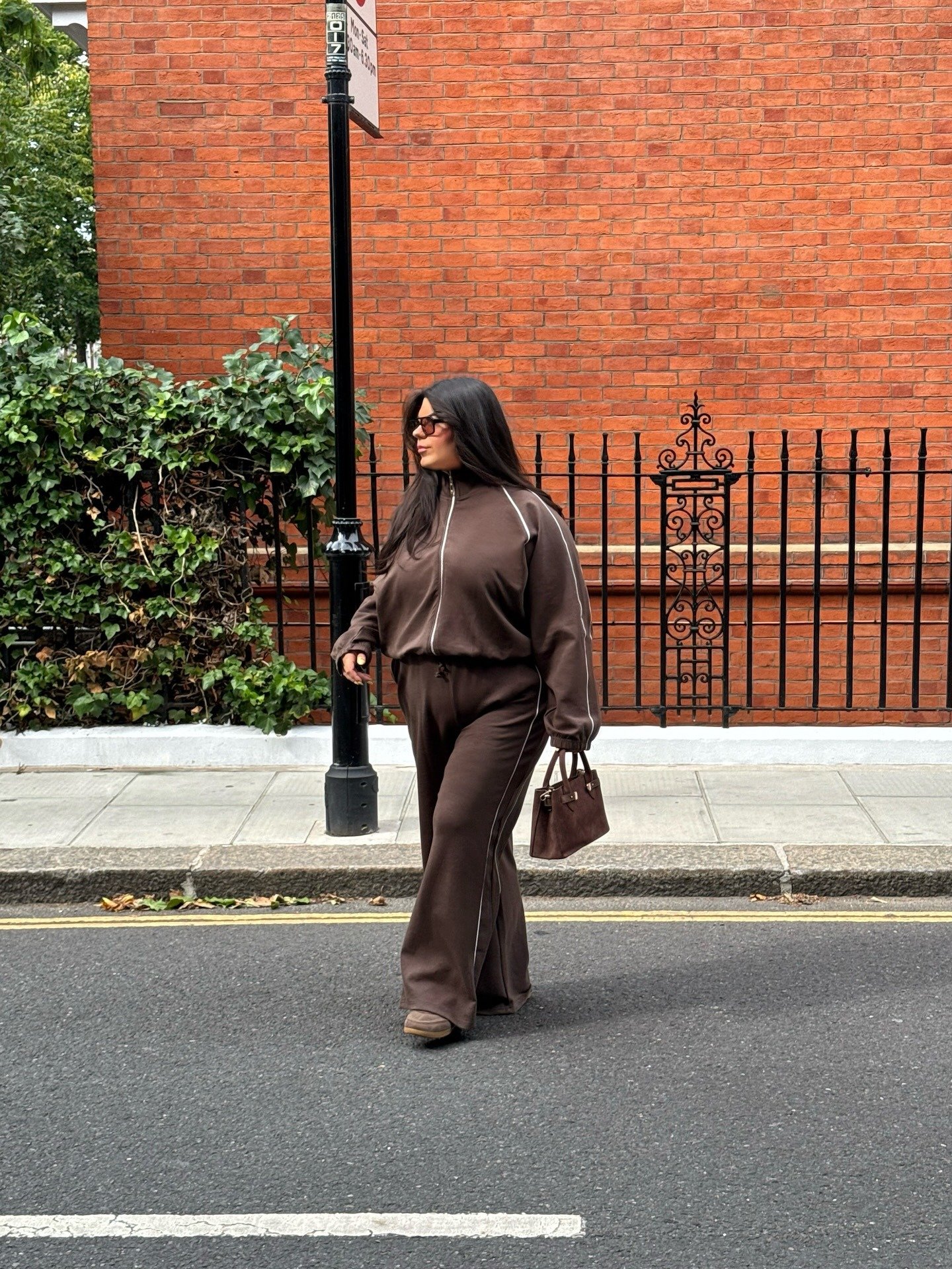 Modelo caminha com ideias de looks femininos confortável em conjunto marrom de moletom com zíper e listras branca.