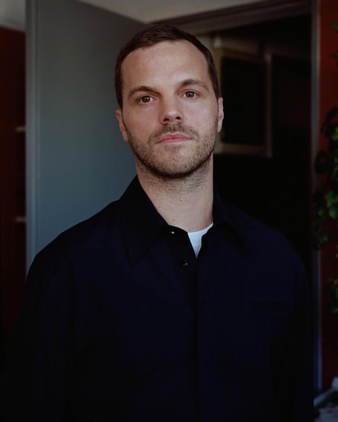 Diretores criativos veste camisa preta de modelagem clássica e transmite serenidade e foco em ambiente interno com luz suave.