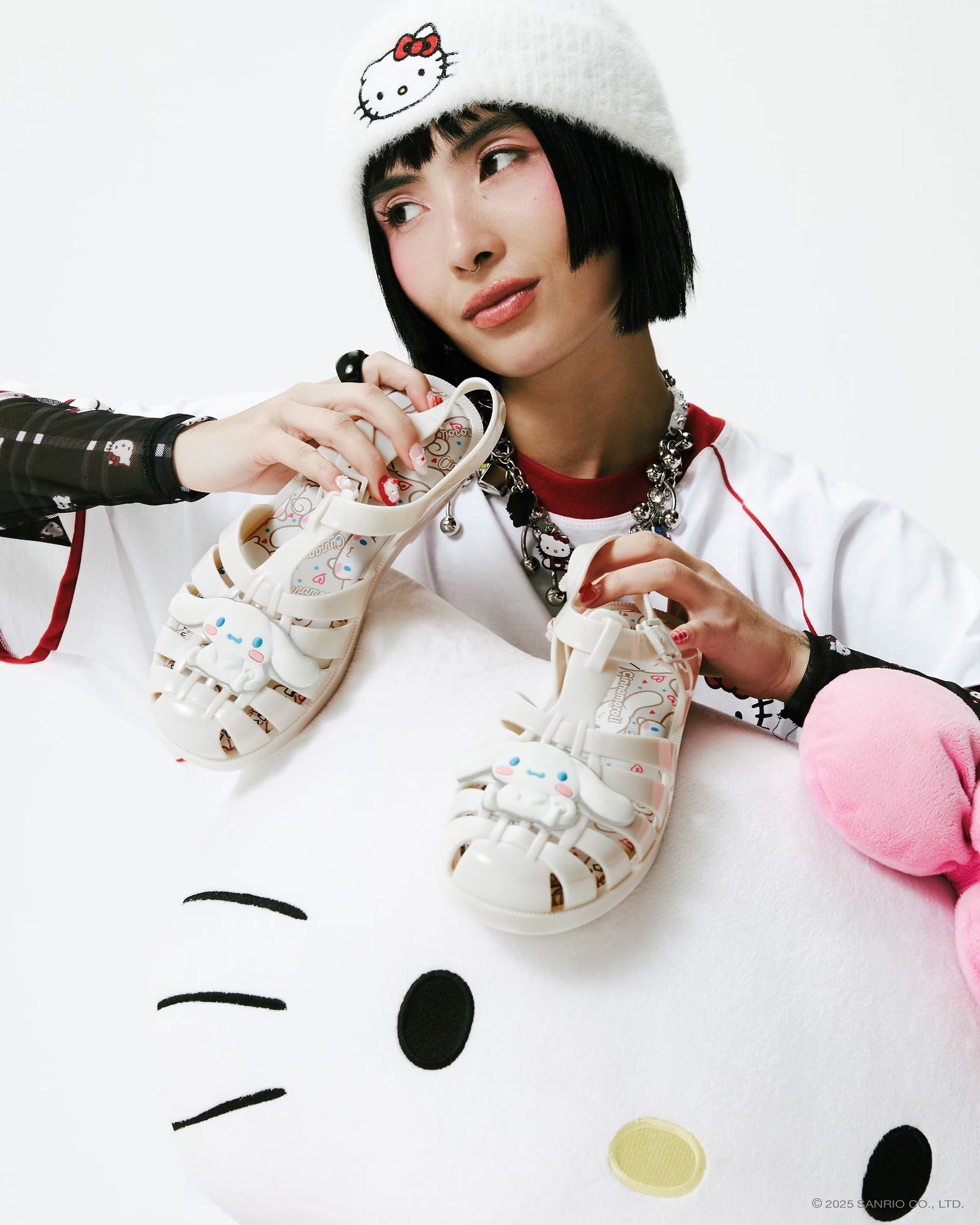 Modelo posa com sandálias de plástico branco com detalhe de personagem fofo, usando blusa branca com manga preta estampada.