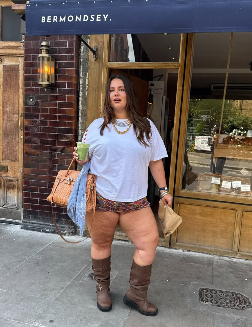 Um look ousado com micro shorts é apresentado, combinando um top oversized branco e botas de cano alto. A escolha de acessórios, como colares e uma bolsa de crochê, adiciona estilo ao visual.