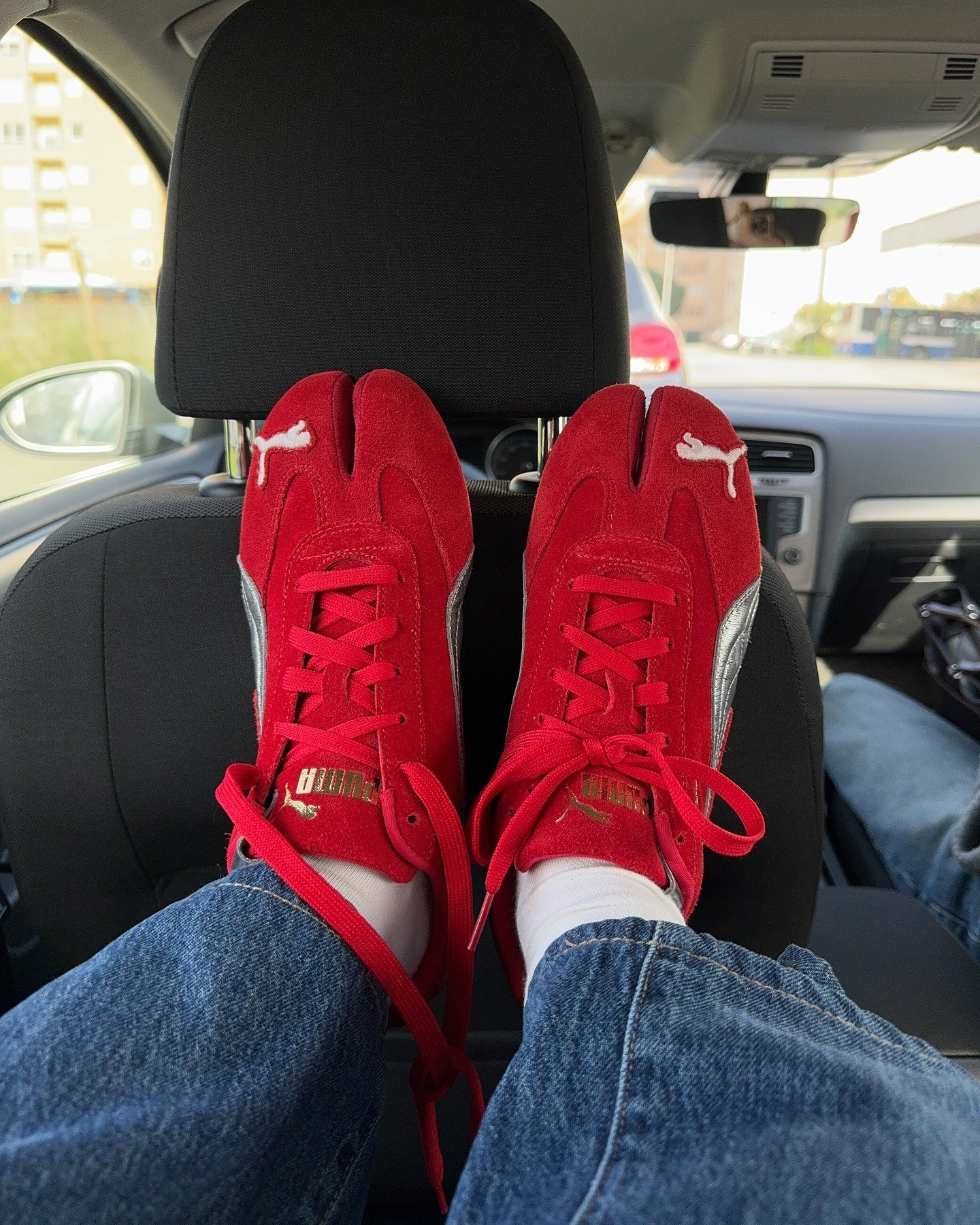 Sapato tabi vermelho em camurça com detalhe prata, modelo casual posa com os pés apoiados no banco dianteiro de carro, clima