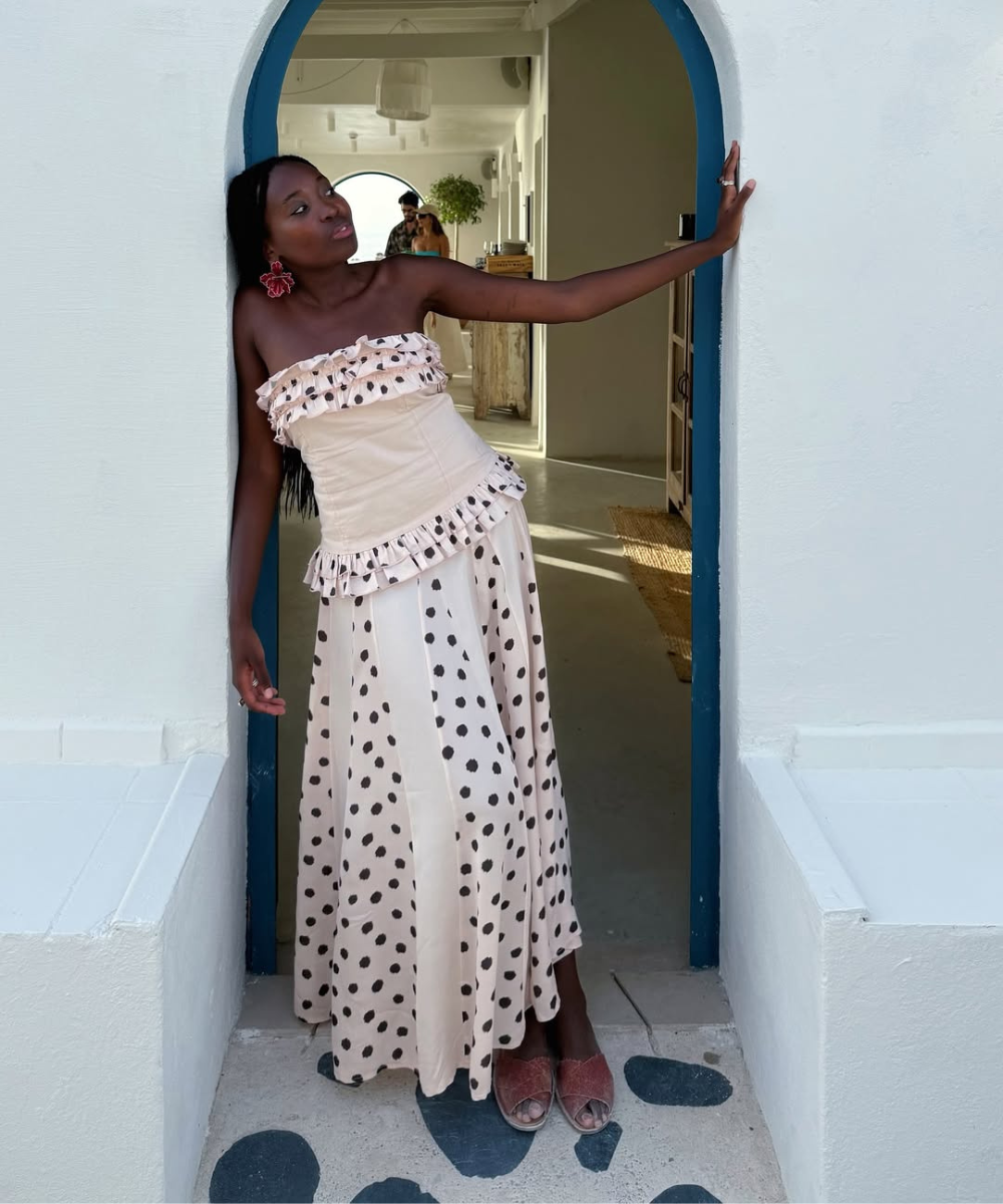 Modelo posa em vestido longo tomara que caia com babados e estampa poá preta sobre fundo bege, ideal para modelos de vestido