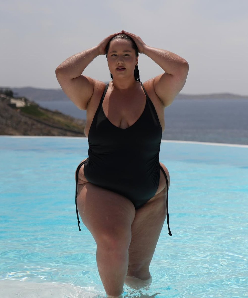 Modelo de maiô adulto em um ambiente de piscina, destacando um maiô preto com design moderno e recortes laterais.