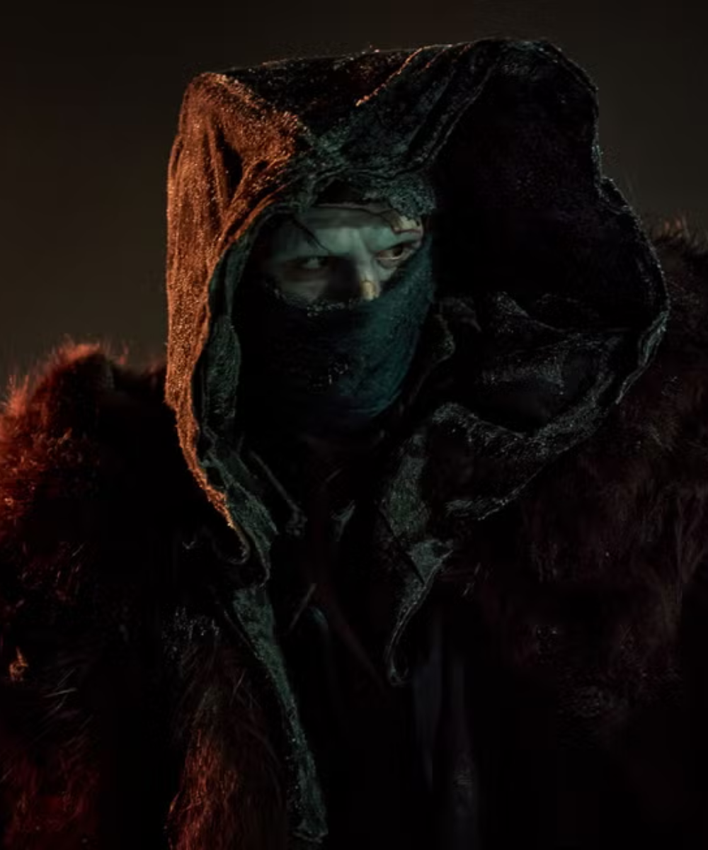 Figurino de Frankenstein com capuz texturizado, máscara preta e casaco de pele escura, criando clima sombrio e misterioso.