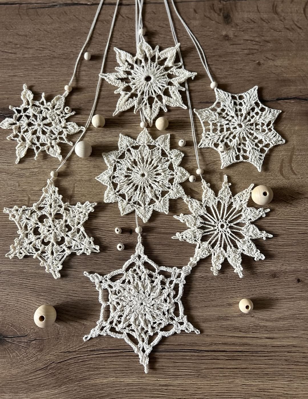 Enfeites de crochê branco com formato de estrelas e bolinhas de madeira clara sobre superfície de madeira rústica.