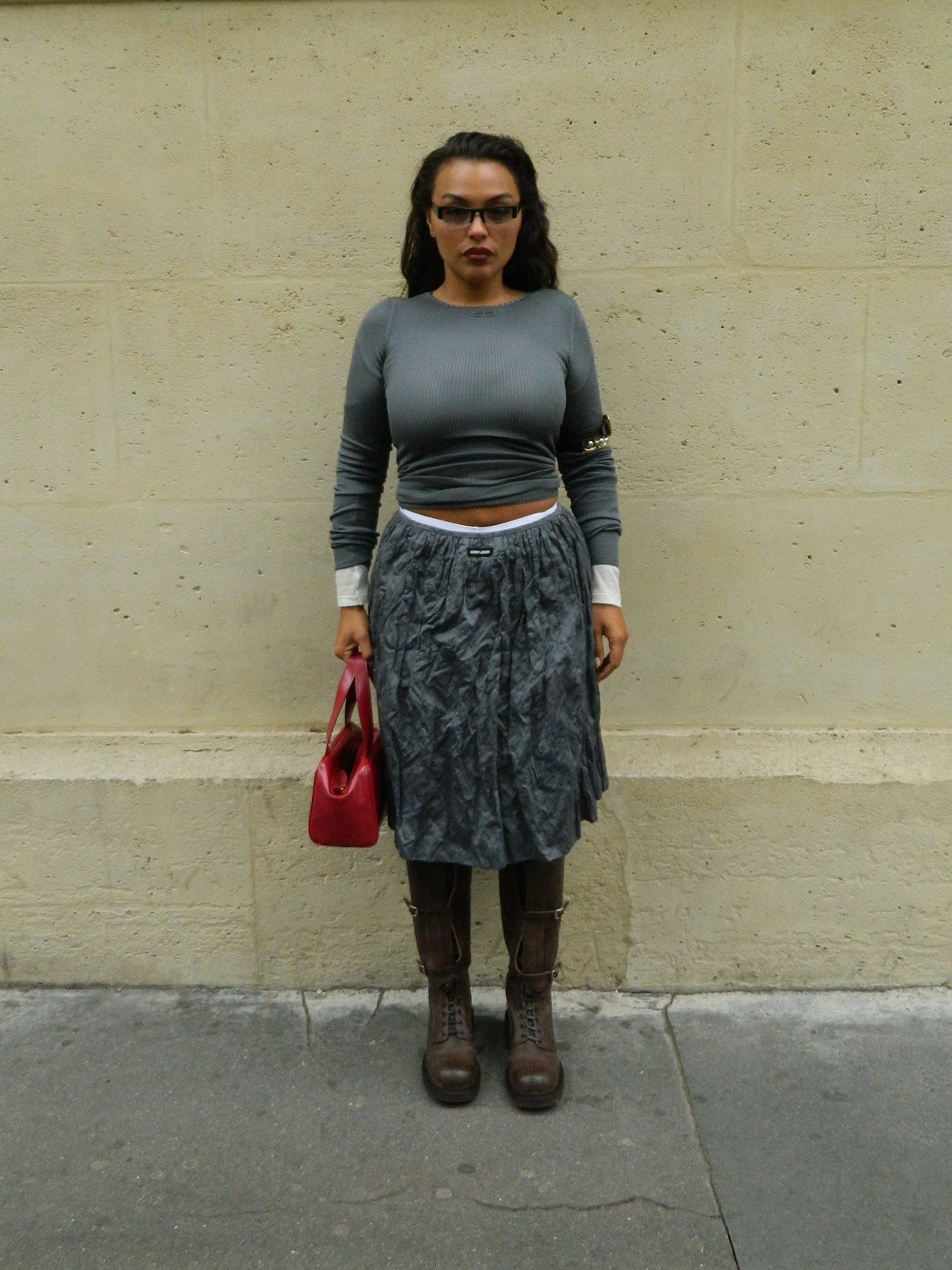 Paloma Elsesser posa com blusa cinza justa de malha canelada, saia texturizada cinza, botas marrons robustas e bolsa