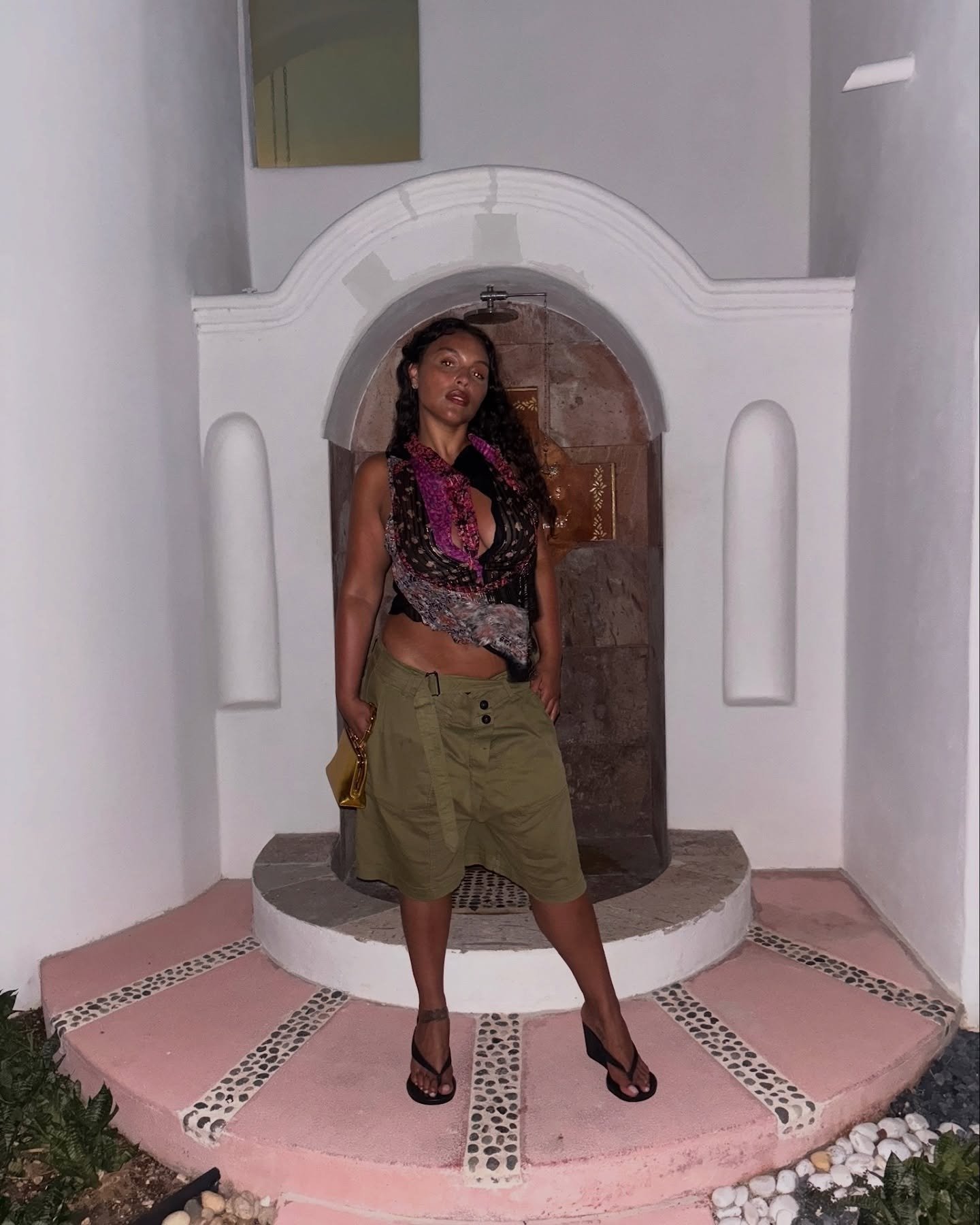 Paloma Elsesser posa confiante com blusa estampada de seda e saia cargo verde, em cenário minimalista com luz suave.