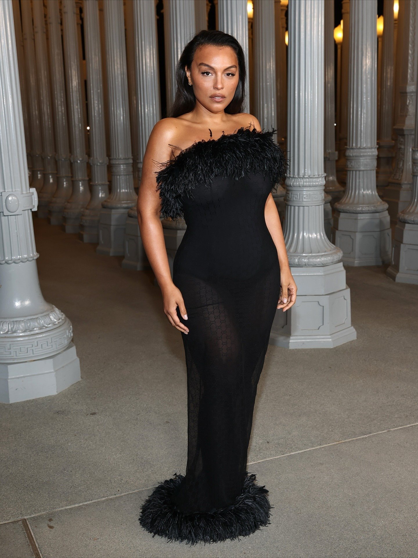 Paloma Elsesser posa confiante com vestido longo preto justo de tule com detalhes em plumas no decote e barra.