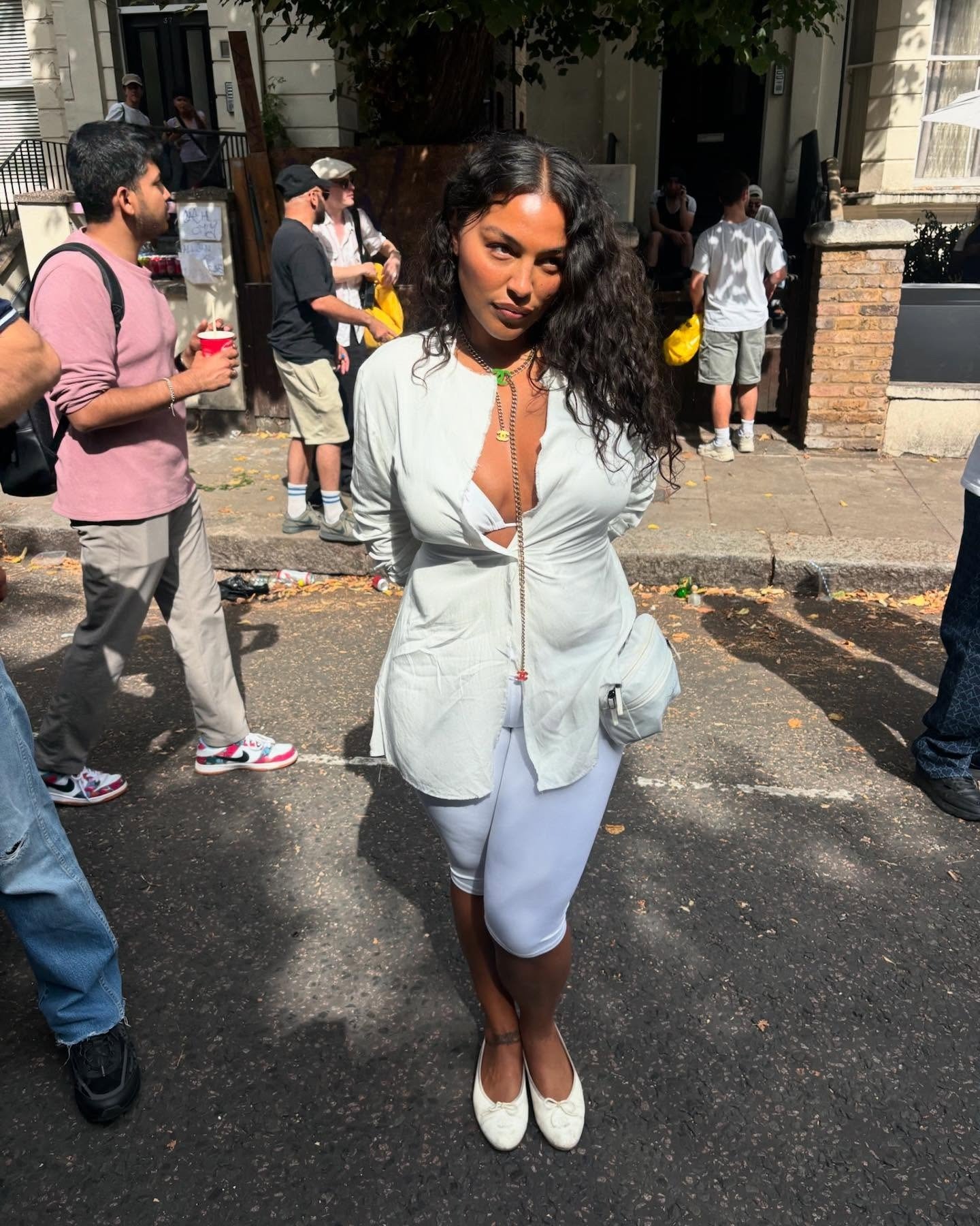 Paloma Elsesser posa com expressão confiante usando blazer branco aberto, top e legging branca justa, com sapatilhas.