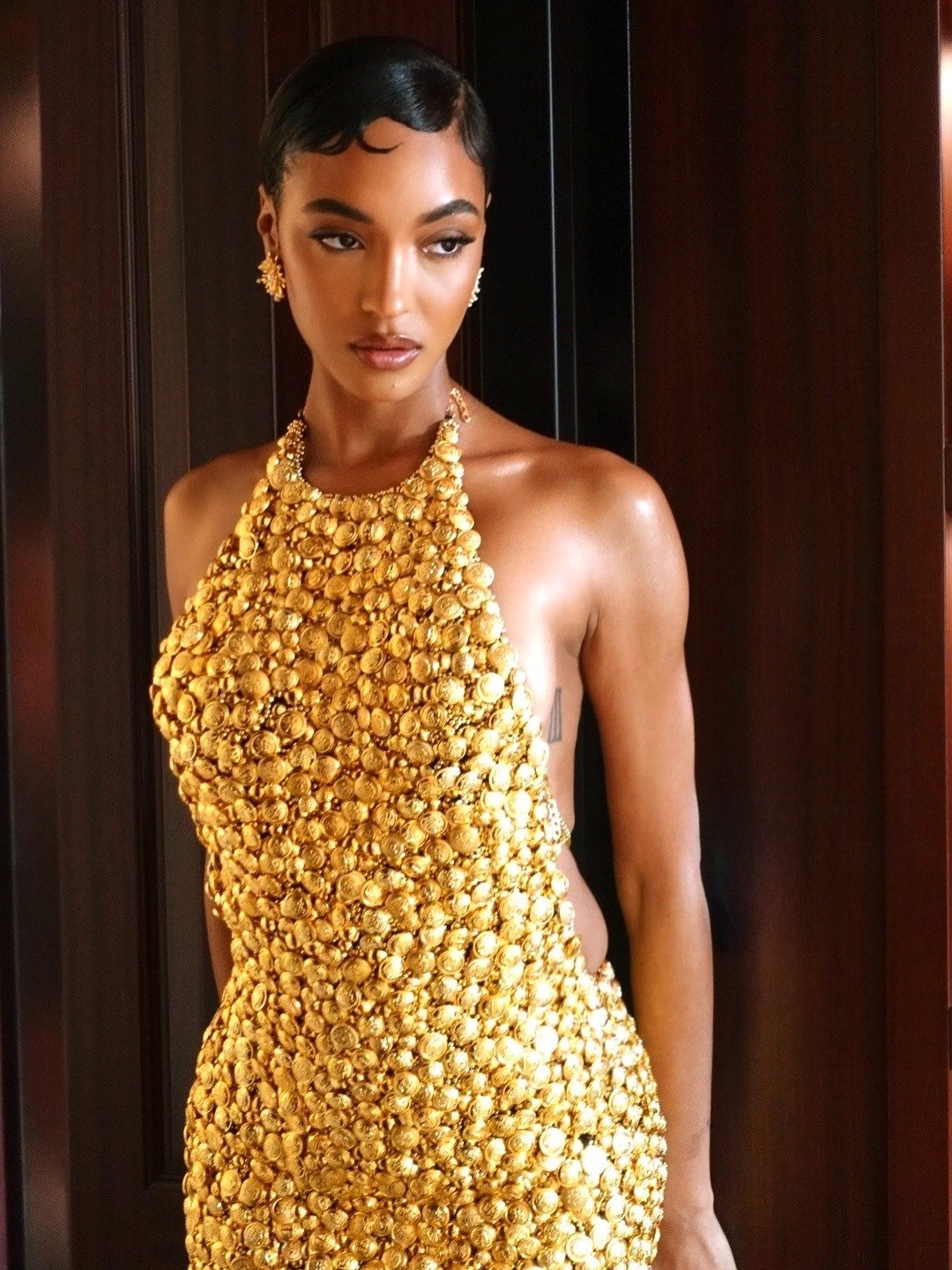 Modelo posa com penteados chiques em fios curtos e estruturados, usando vestido dourado de textura rica e brilho intenso,