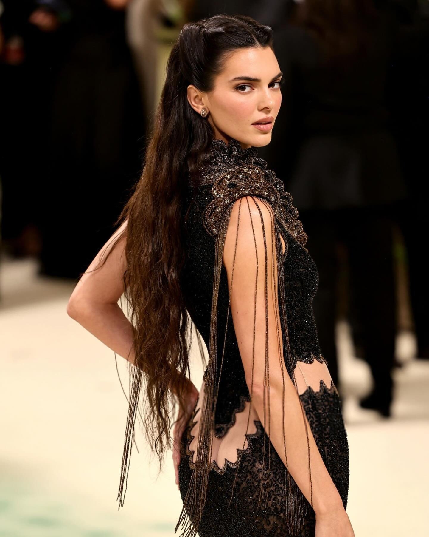 Modelo posa com penteado chique de cabelo longo semi preso e ondulado, vestido preto com detalhes em renda e franjas