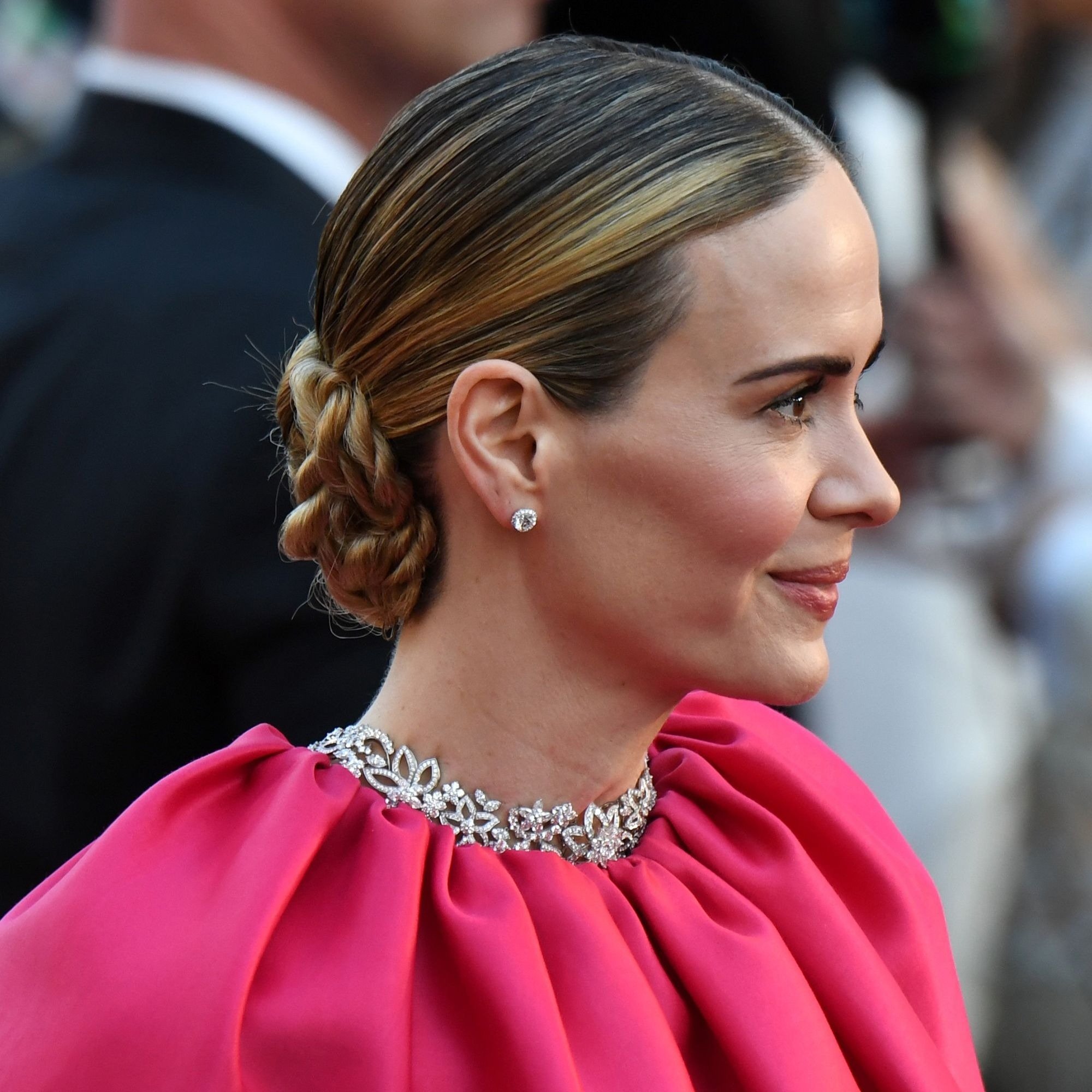 Penteado chique com coque trançado e cabelo liso preso, combinado com vestido pink vibrante e colar de pedras brilhantes,