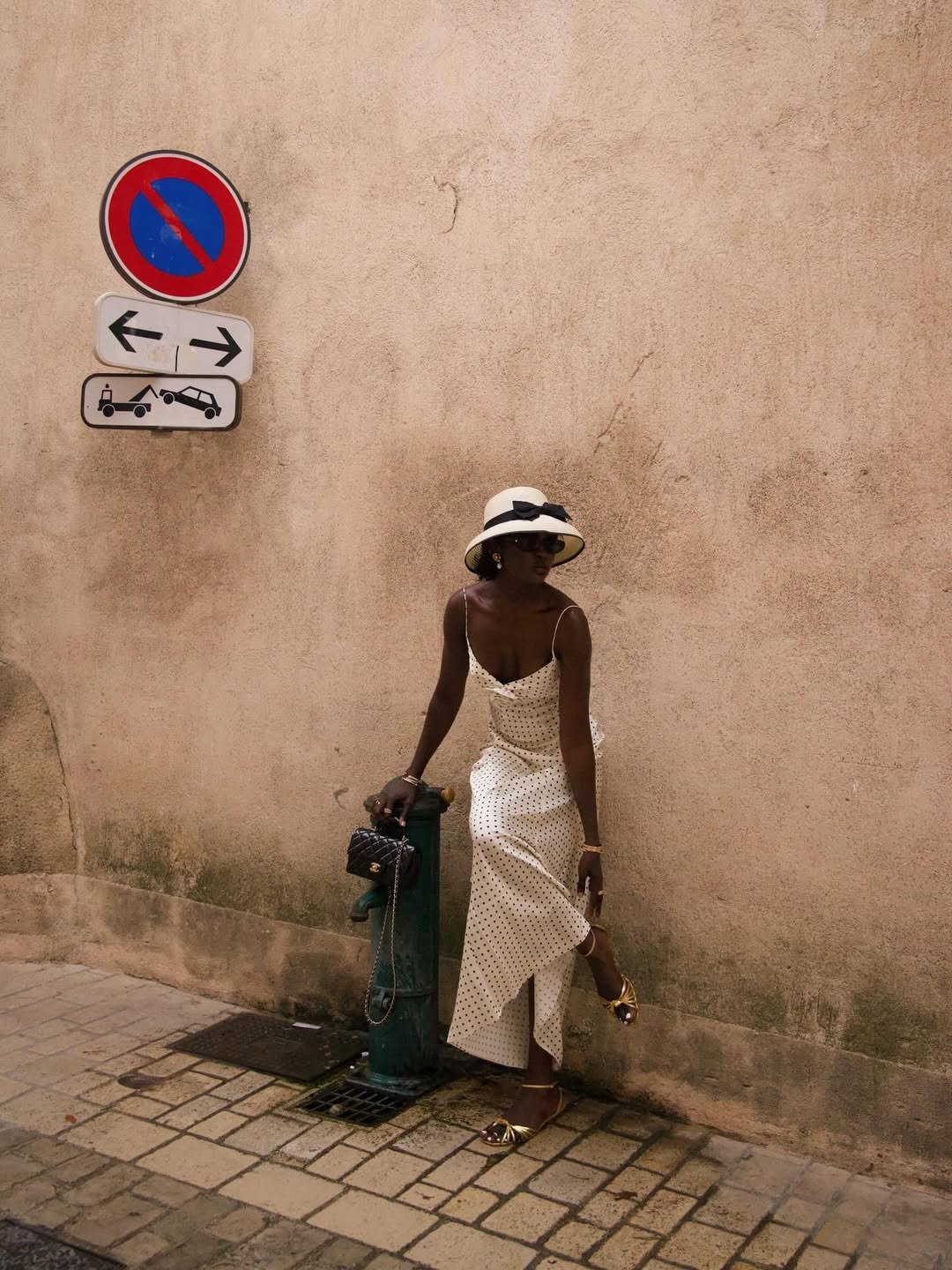 A rasteirinha dourada brilha em meio ao look elegante, que combina um vestido branco com poás e um chapéu sofisticado. A composição é perfeita para um dia de verão, destacando a leveza e o estilo.