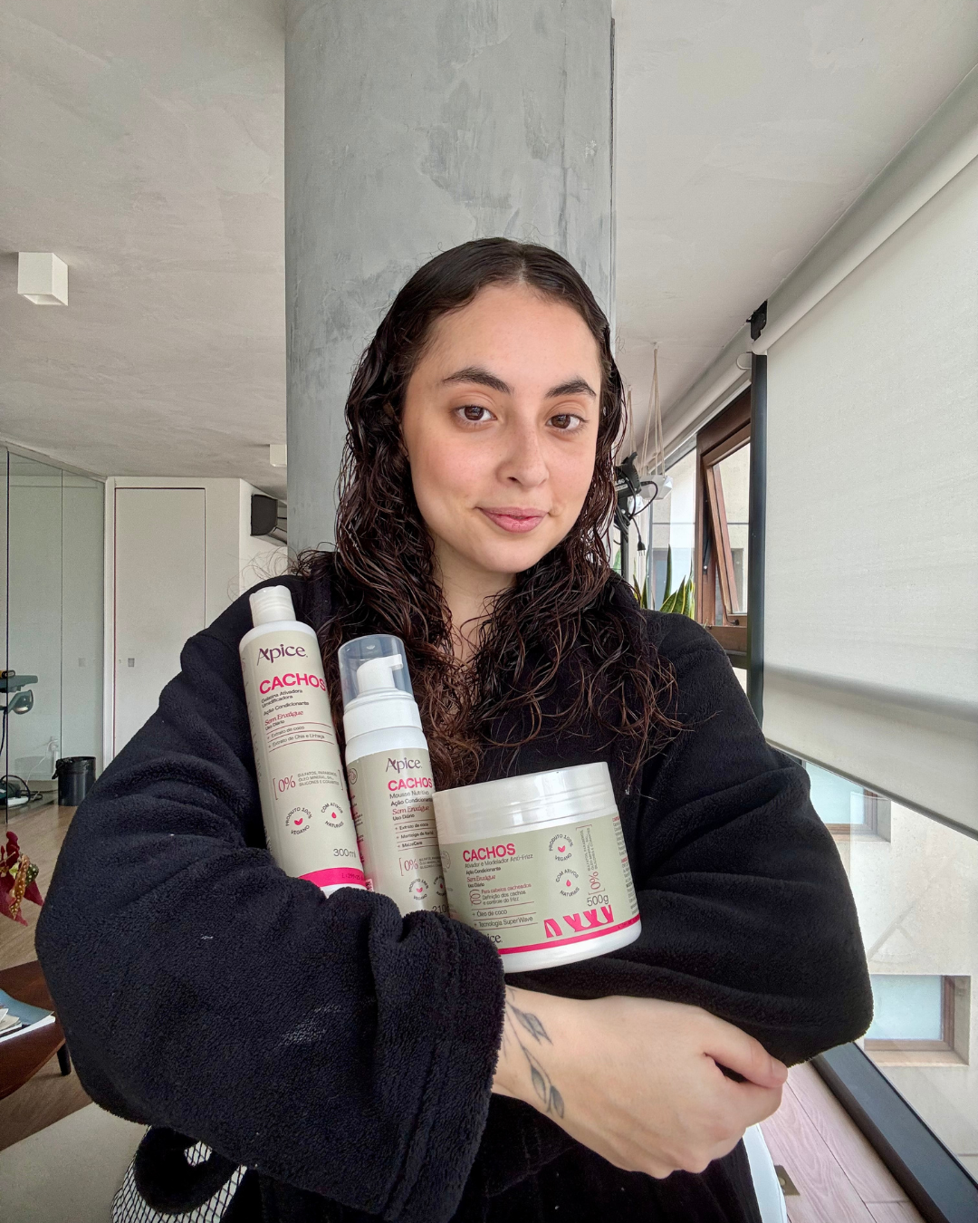 Modelo com cabelo cacheado úmido, veste roupão preto e destacando rotina para cabelo cacheado por menos de 200 reais