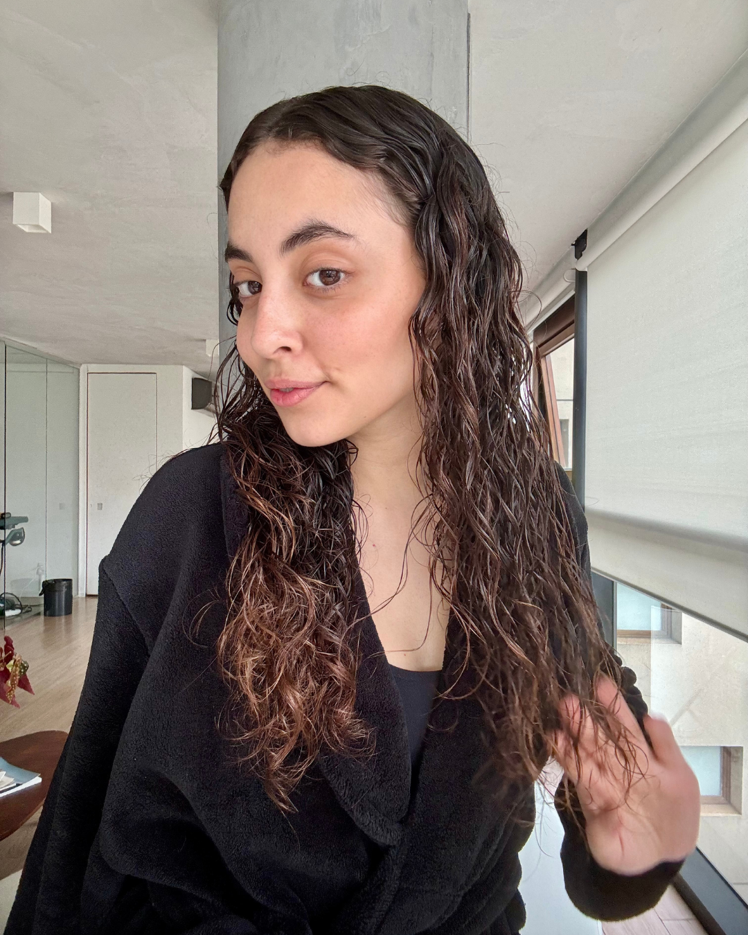 Mulher com cabelo cacheado úmido, veste roupão preto de tecido macio, com rotina para cabelo cacheado por menos de 200 reais